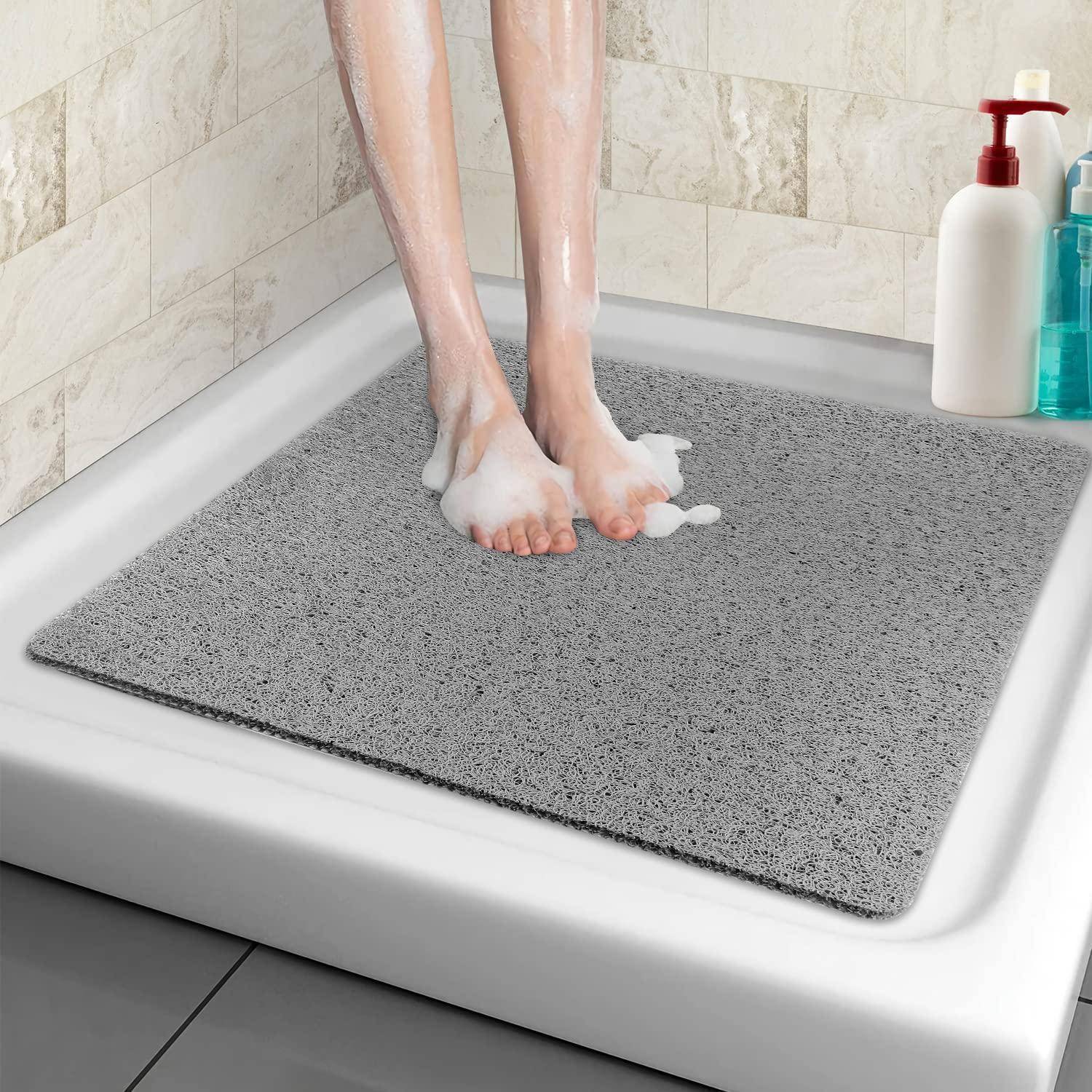 Person, die auf einer grauen Badmatte in einer Dusche steht, mit Seifenschaum an Füßen und Beinen.