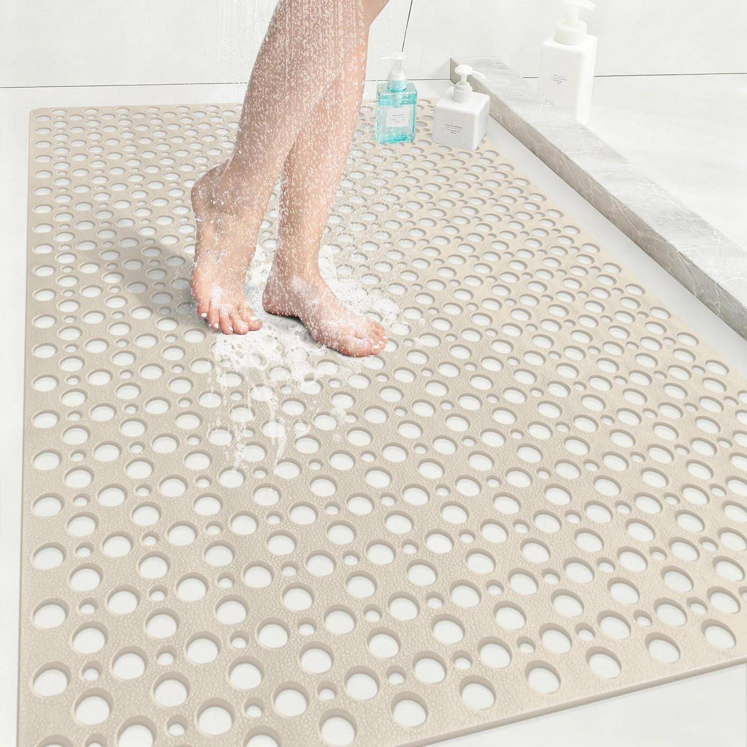 Füße stehen auf einer beigen, gelöcherten Badematte in einem Badezimmer mit Wasser und Seifenflaschen in der Nähe.
