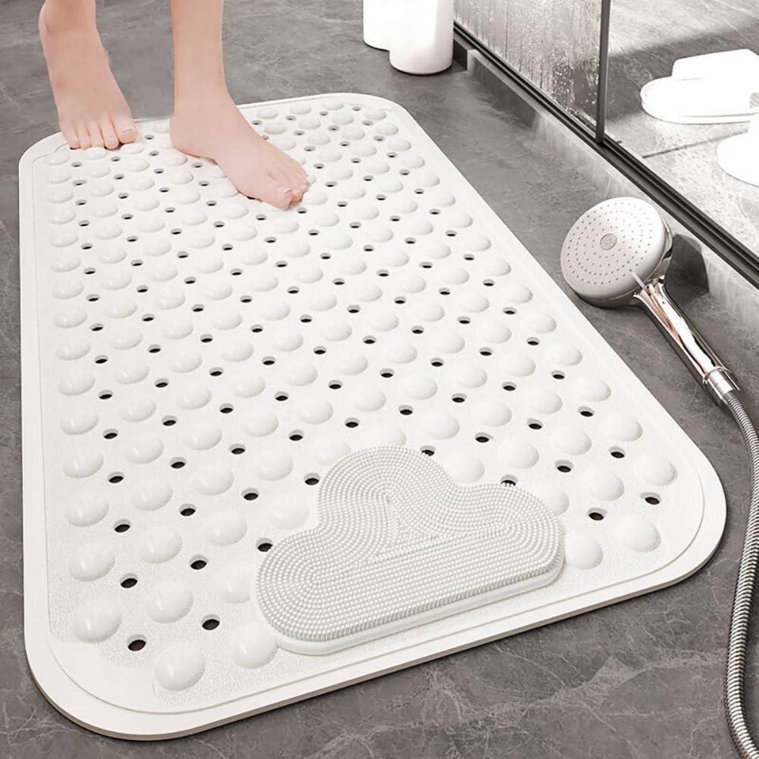 Füße stehen auf einer weißen strukturierten Badematte mit Ablöchern neben einem Handbrausekopf auf einem Badezimmerboden.