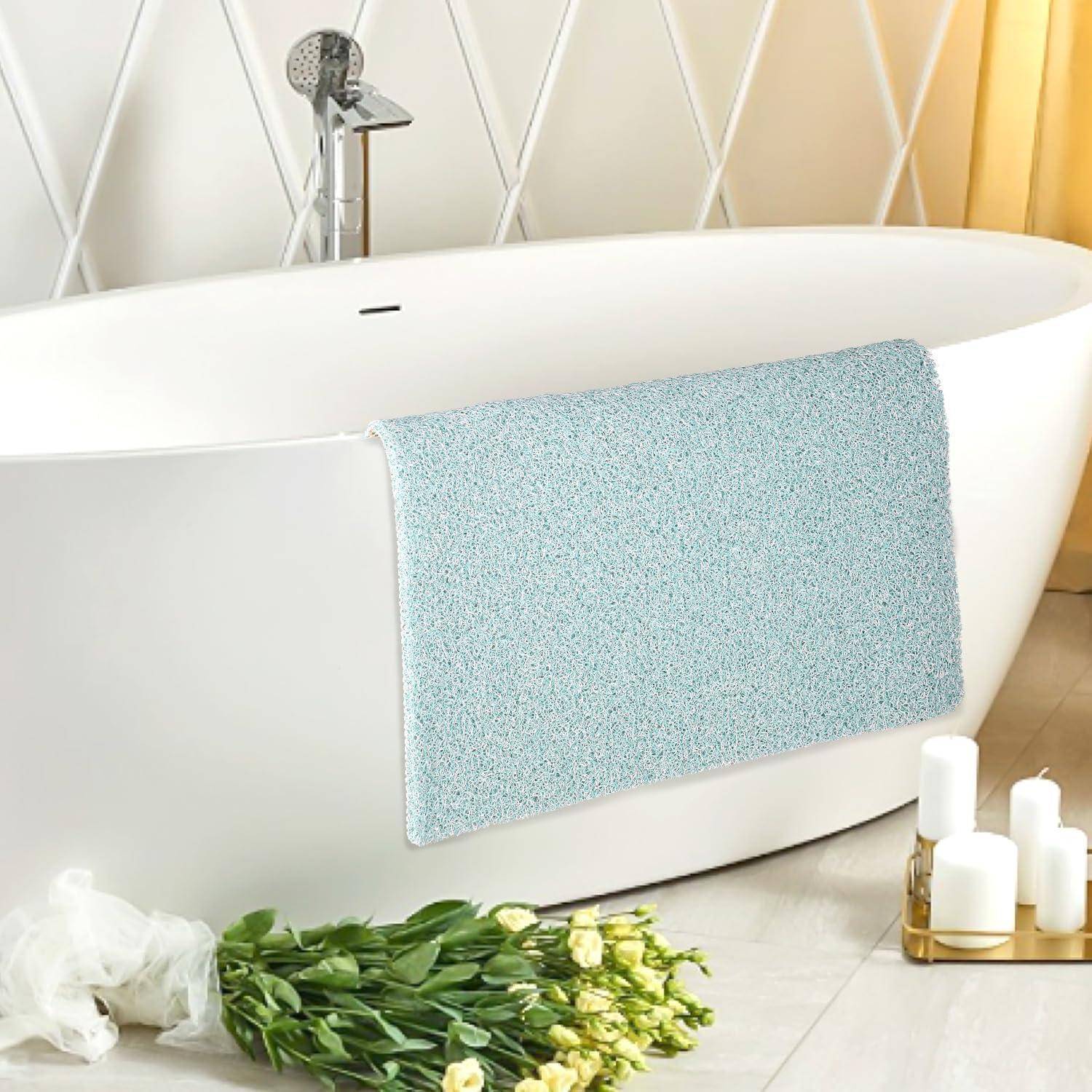 Moderne freistehende weiße Badewanne mit Duscharmatur, drapiert mit einer blauen Badematte; Strauß weißer Blumen und Kerzen auf dem Boden.