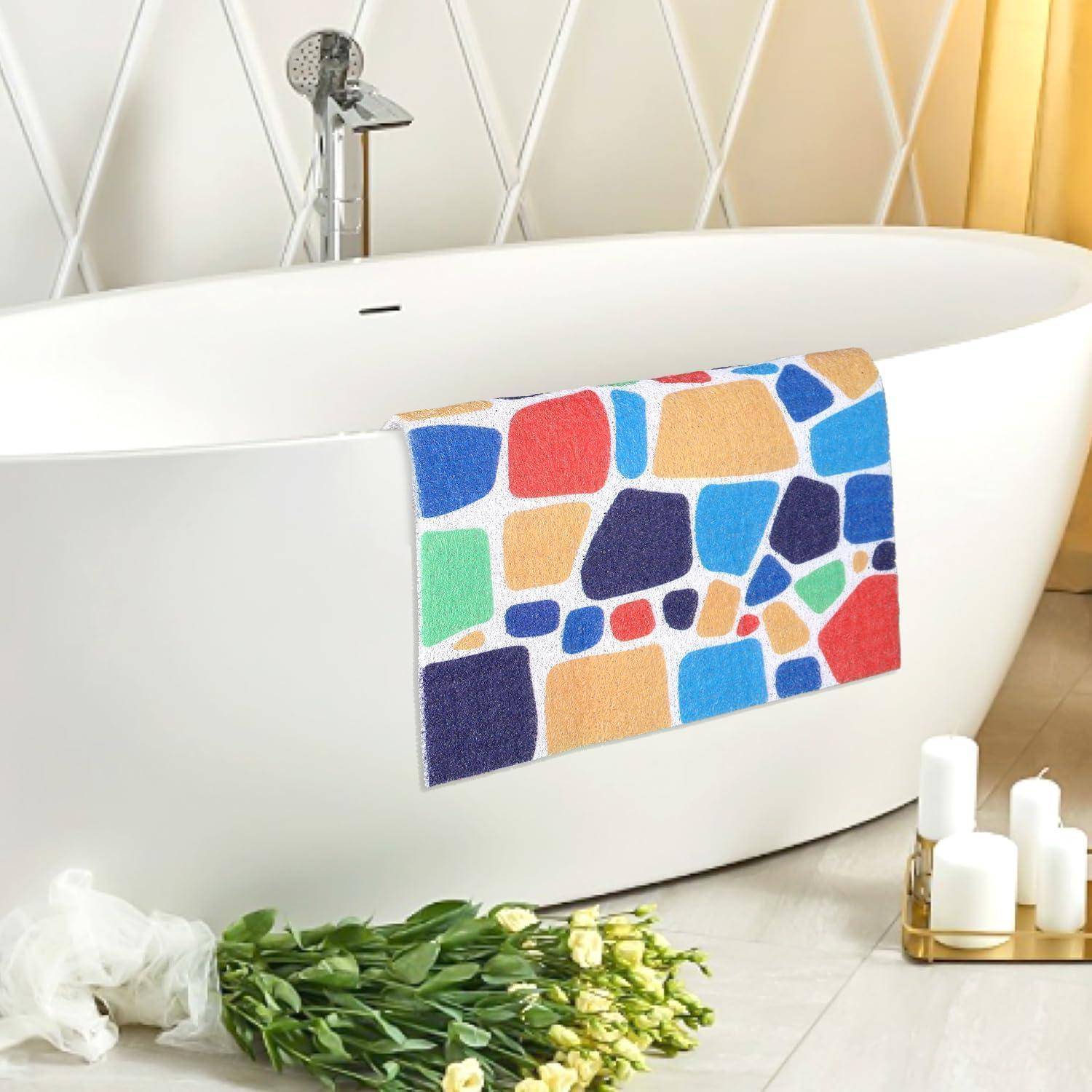 Moderne freistehende weiße Badewanne mit einer farbenfrohen geometrischen Badematte, die über die Seite drapiert ist, neben Blumen und Kerzen in einem spa-ähnlichen Badezimmer.