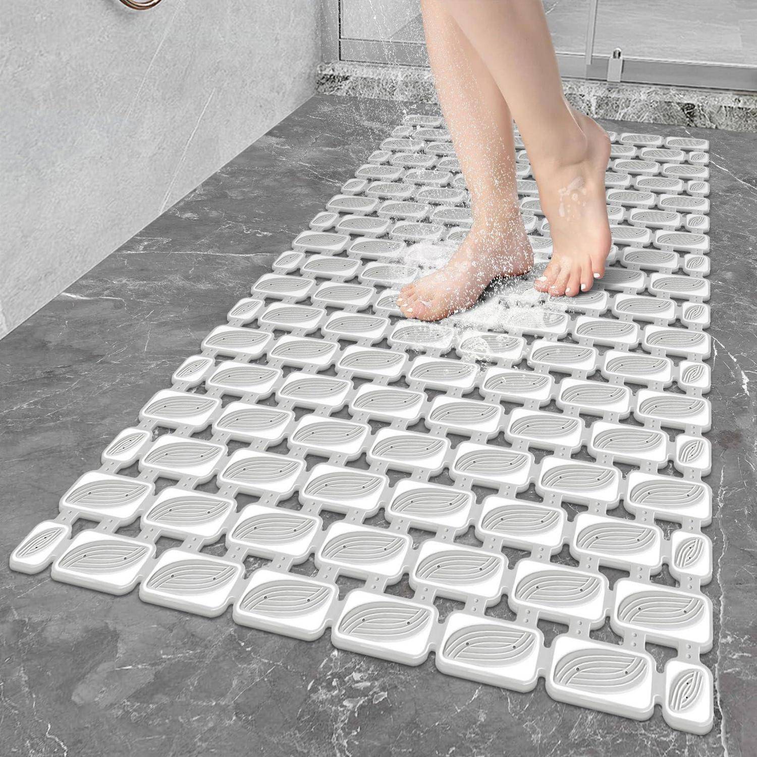 Füße stehen auf weißen ineinandergreifenden Duschmattenelementen in einem feuchten Badezimmer und zeigen eine rutschfeste Drainagenoberfläche unter fließendem Wasser.