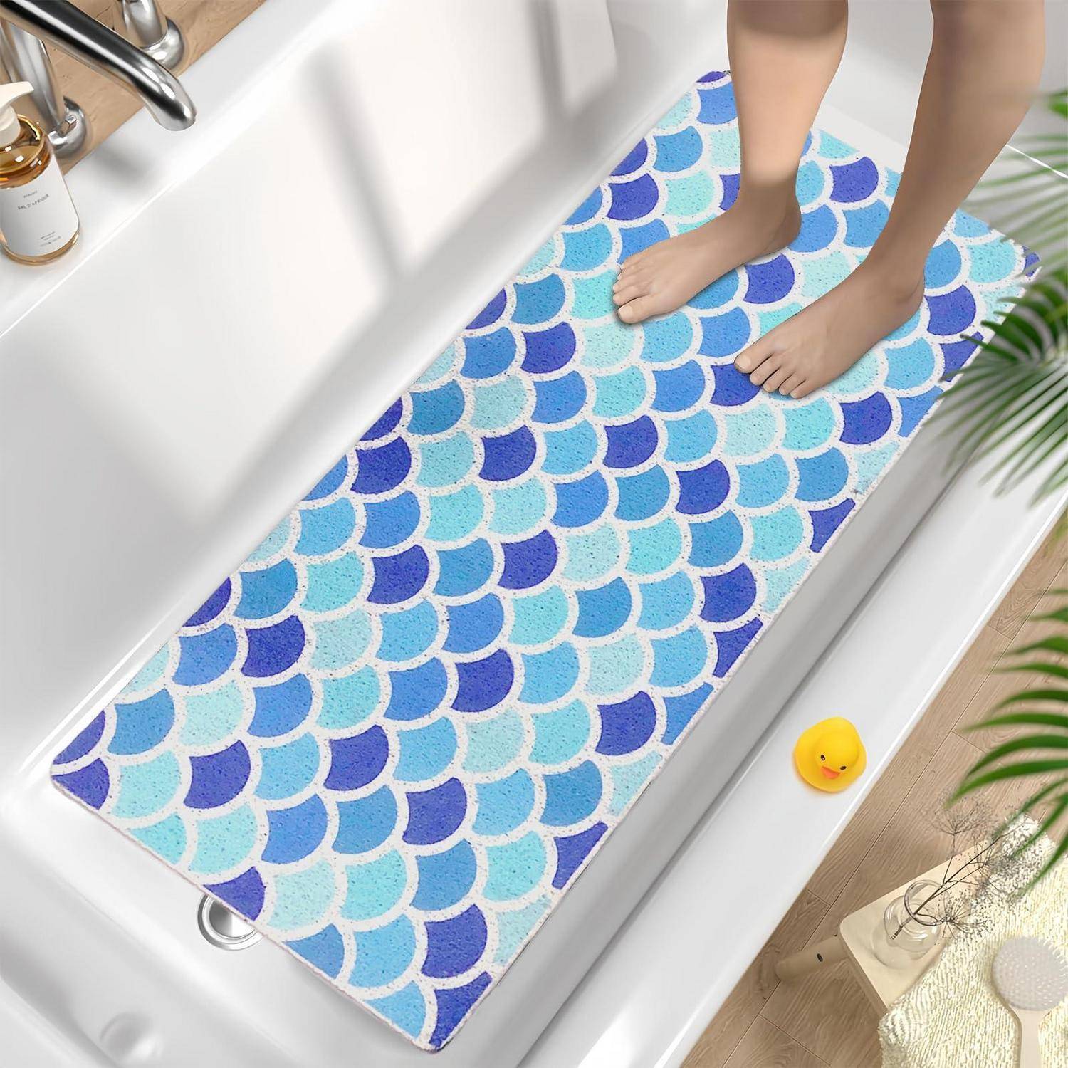 Nackte Füße, die auf einer blauen Badewannenmatte mit Fischschuppenmuster stehen, die über einer weißen Badewanne ausgebreitet ist.