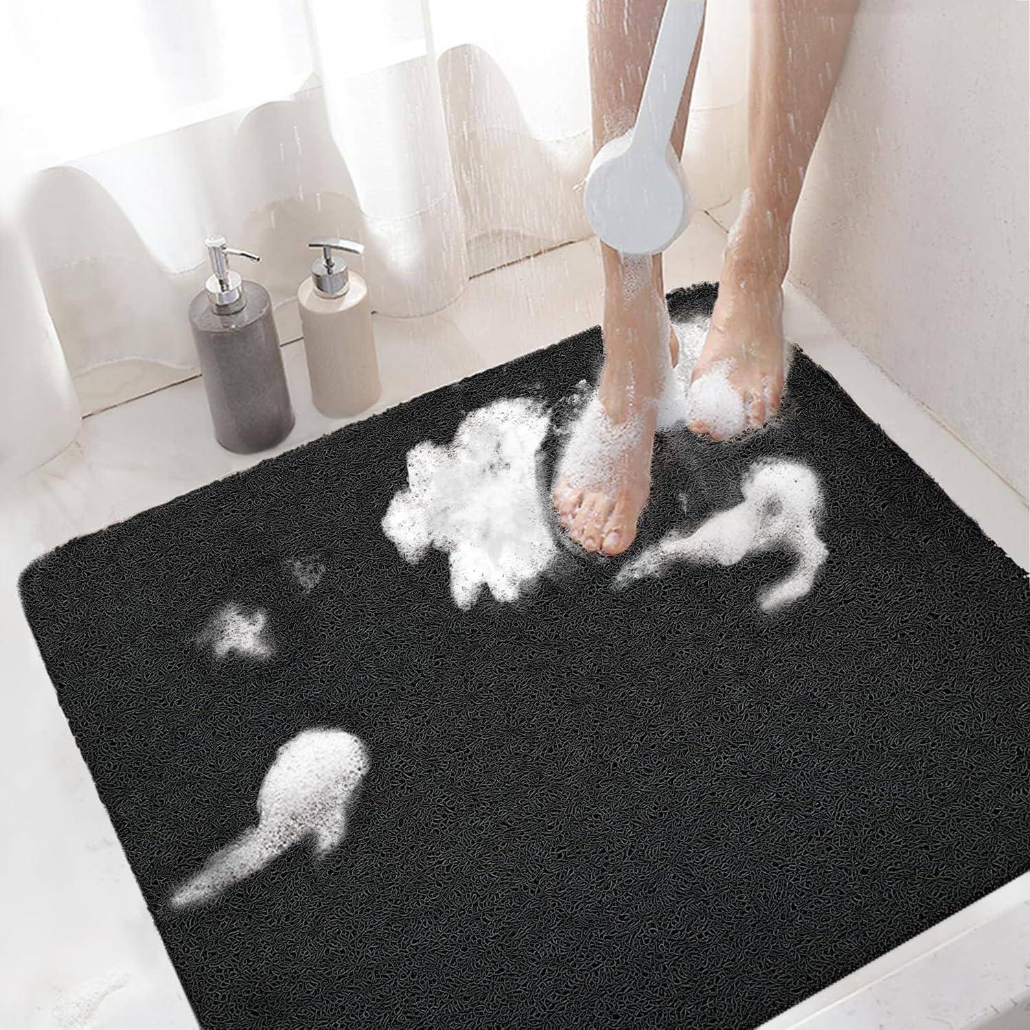 Person, die auf einer schwarzen Badmatte duscht, mit Seifenschaum; Shampoo- und Körperwaschflaschen stehen neben der Dusche.