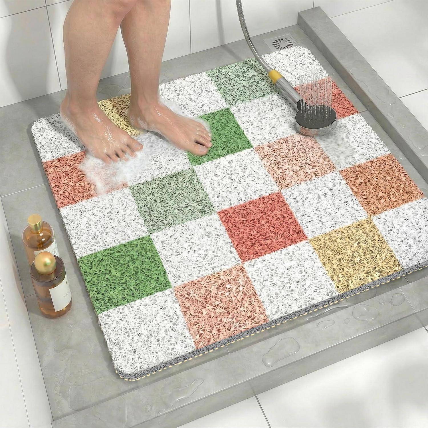 Eine Person wäscht sich die Füße auf einer karierten Badewannenmatte in einer Dusche, mit einer Handbrausekopf und Toilettenartikeln in der Nähe.