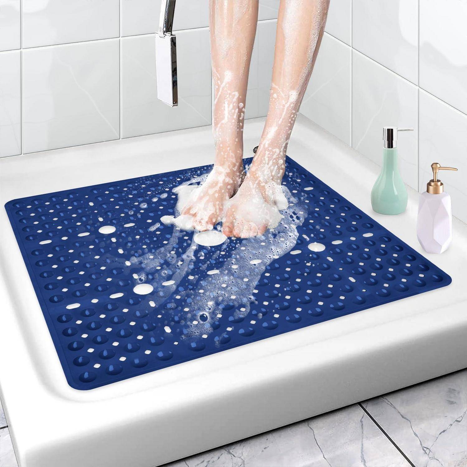 Person wäscht Füße auf einer blauen rutschfesten Badewannenmatte in einer Dusche oder Badewanne, mit Seifenschaum und Badezimmerartikel in der Nähe.