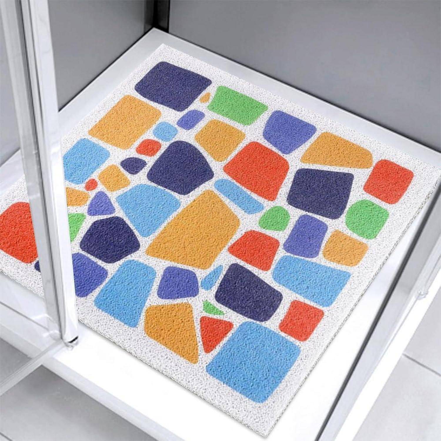 Farbenfrohe, kieseltexturierte Badematte mit mehrfarbigen geometrischen Formen auf einem weißen Badezimmerboden.