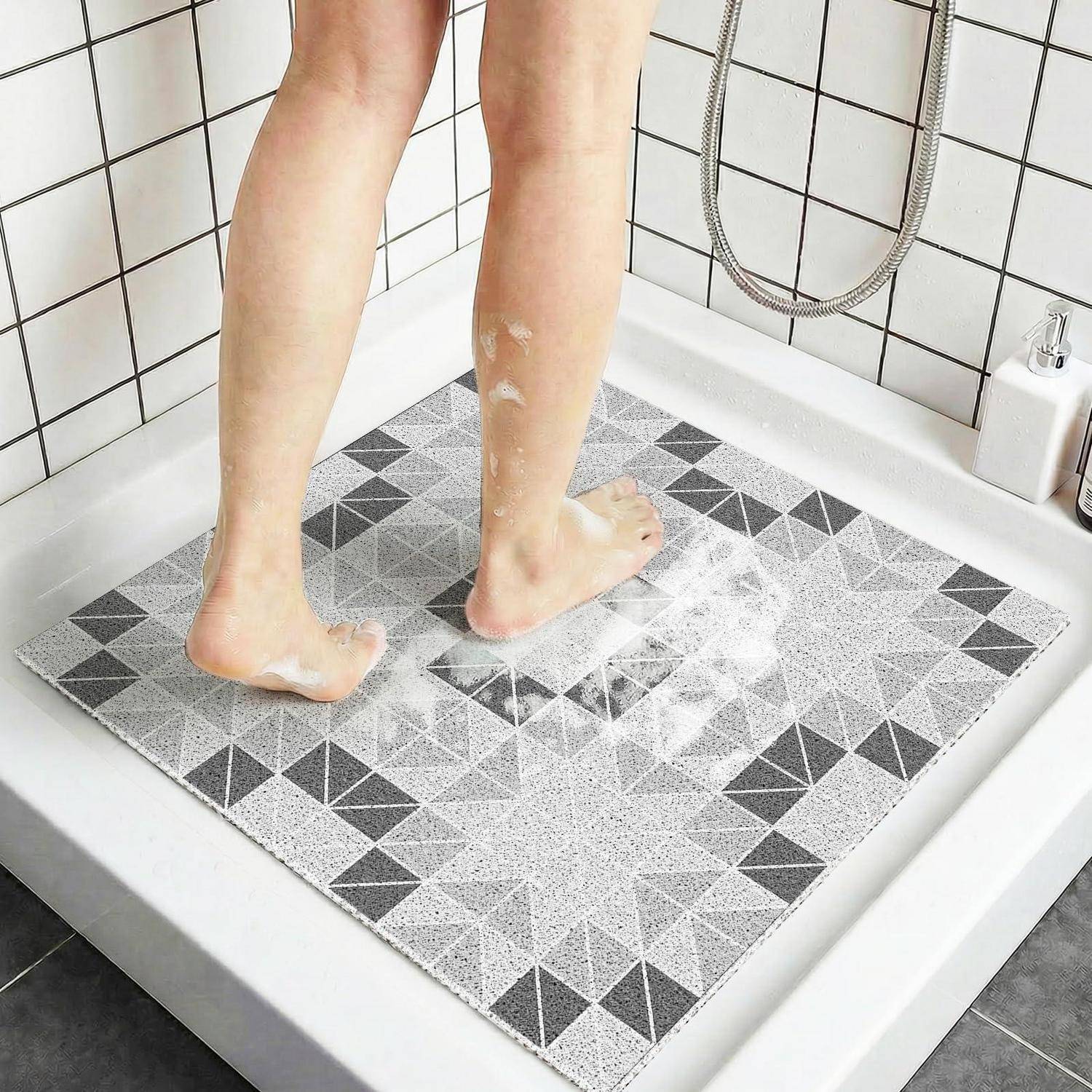 Eine Person steht in einer Dusche auf einer grauen geometrischen Badematte mit Seifenschaum an ihren Beinen und Füßen.