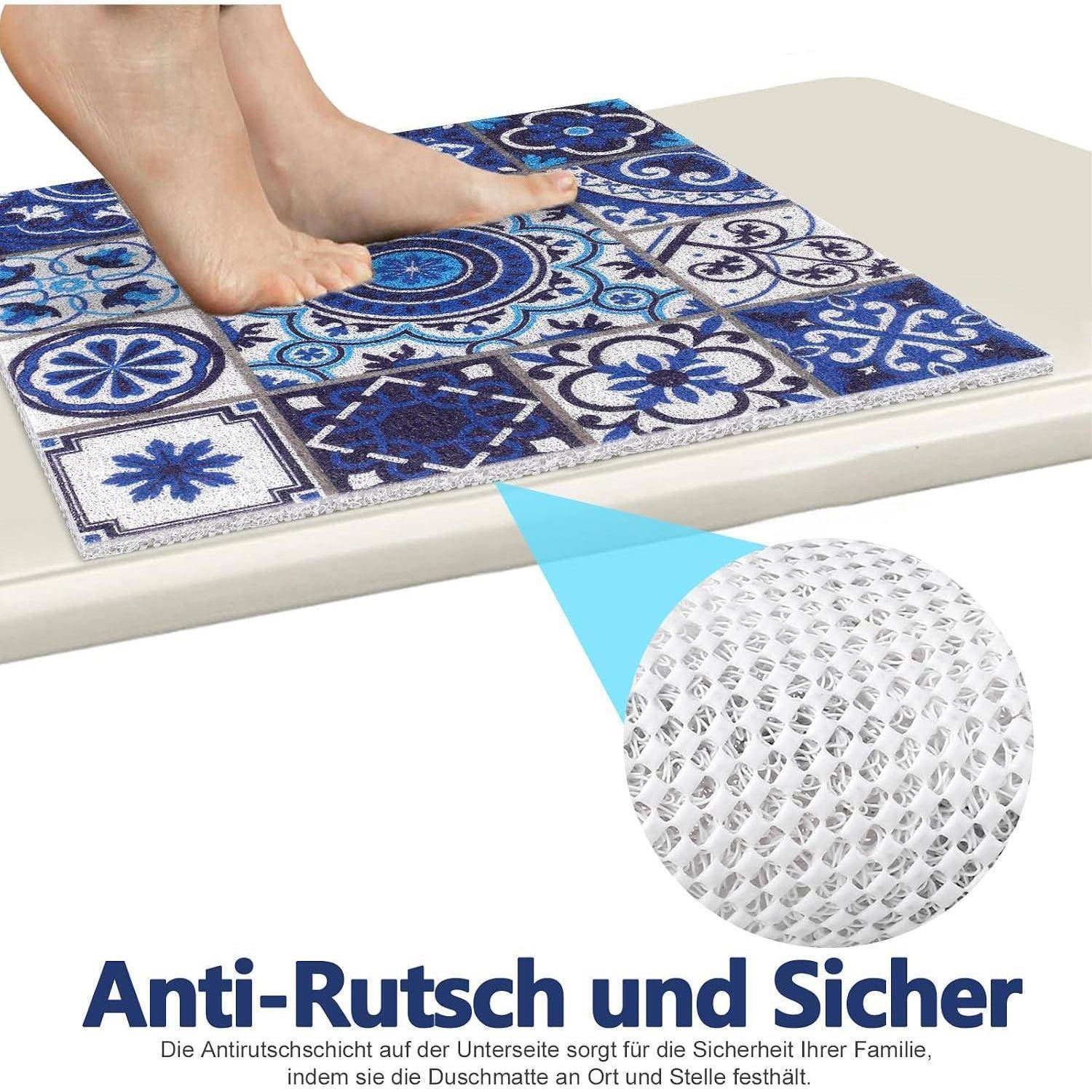Nackte Füße stehen auf einer blauen gemusterten Matte auf einem Fliesenboden; eine Vergrößerung zeigt die rutschfeste Unterseite mit deutschem Text „Anti-Rutsch und Sicher".