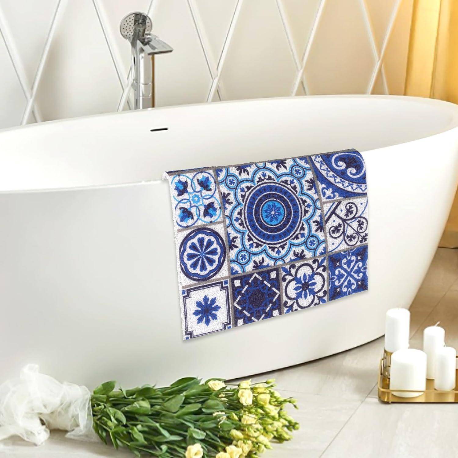 Moderne freistehende weiße Badewanne mit blauem Fliesenmuster, das über die Seite drapiert ist, neben weißen Kerzen und einem Blumenstrauß auf dem Boden.