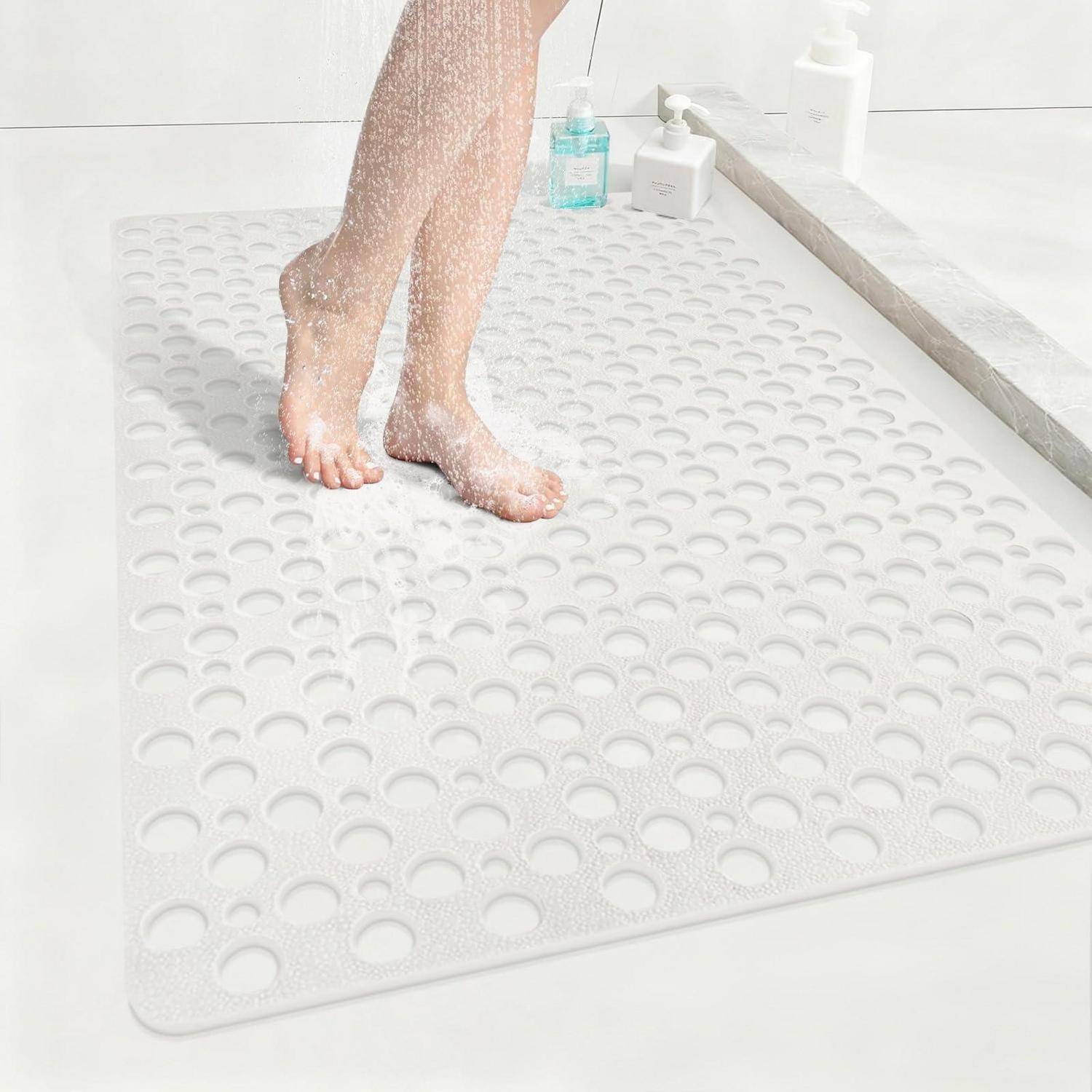 Person, die auf einer weißen strukturierten rutschfesten Badewanne auf einer Badewanne duscht, mit Füßen, die in Seifenschaum bedeckt sind, und Toilettenartikeln in der Nähe.