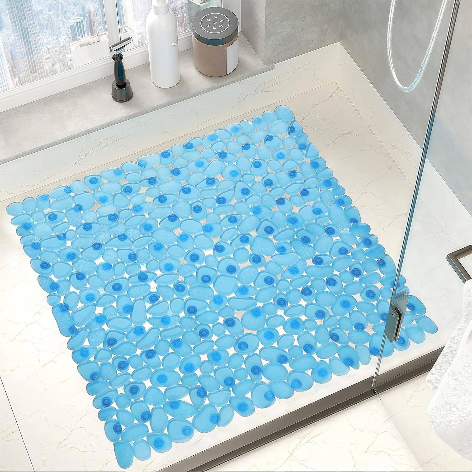 Blaue Kieselstein-Badmatte auf einem weißen Duschboden in einem modernen Badezimmer, fotografiert durch eine Glastür der Duschkabine.