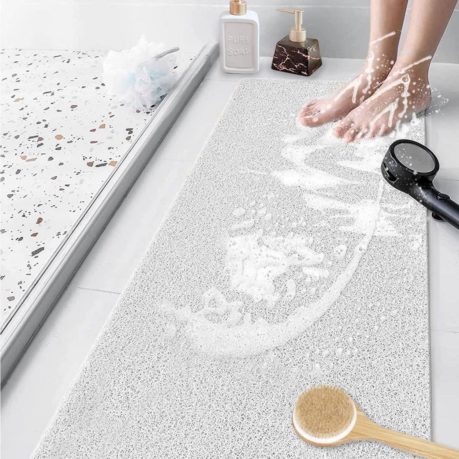Nackte Füße waschen eine strukturierte Badevorlage in einer Dusche, mit Seifenschaum, einem Handbrausekopf und Badezubehor in der Nähe.