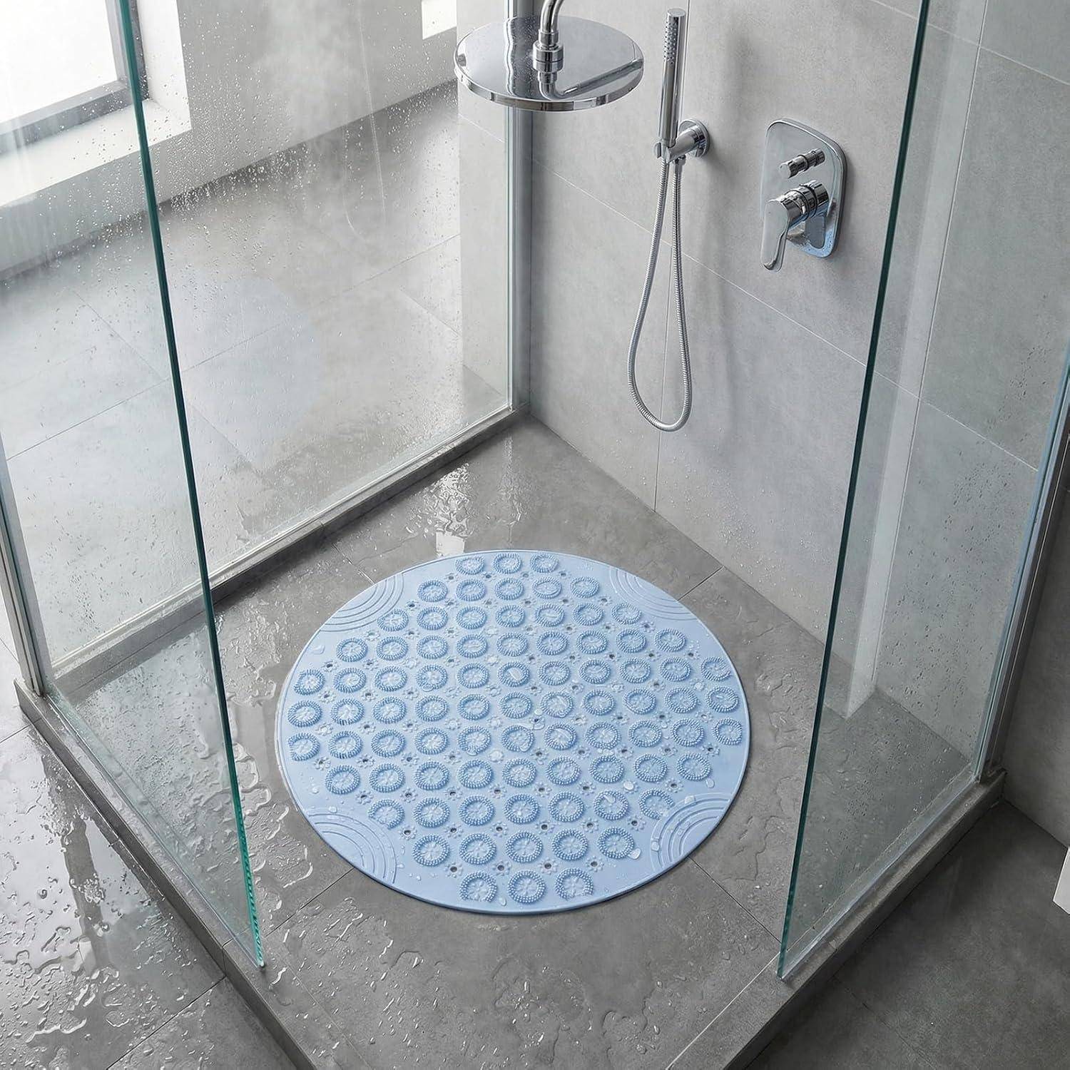 Modernes begehbares Duschbad mit Glaspaneelen, wandmontierter Dusche und rundem hellblauem rutschfestem Badevorleger auf nassem grauem Fliesenboden.