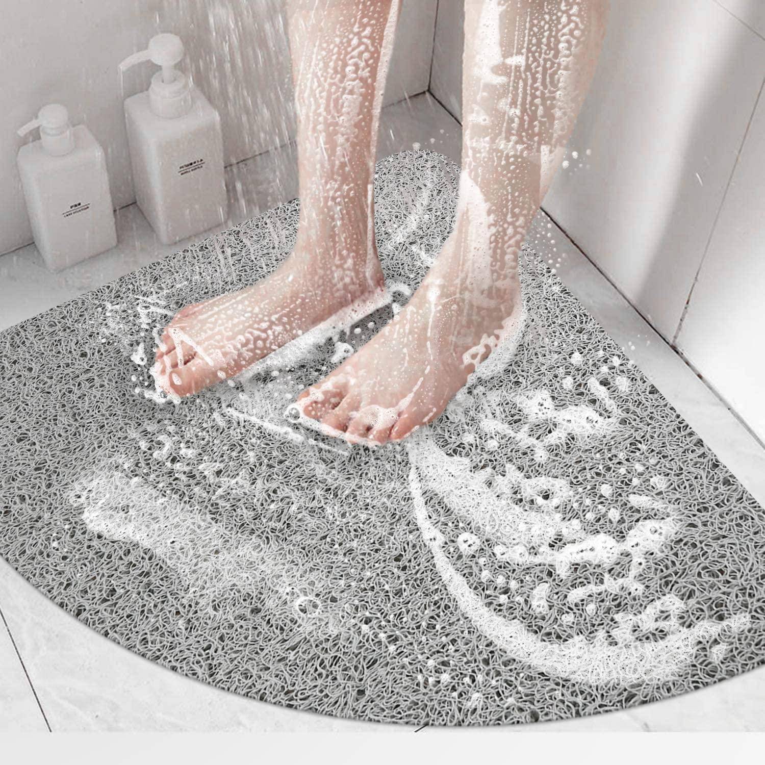 Füße, die auf einer strukturierten grauen Badematte stehen, während Wasser und Seife in einer Dusche abgespült werden; Shampooflaschen sitzen in der Ecke.