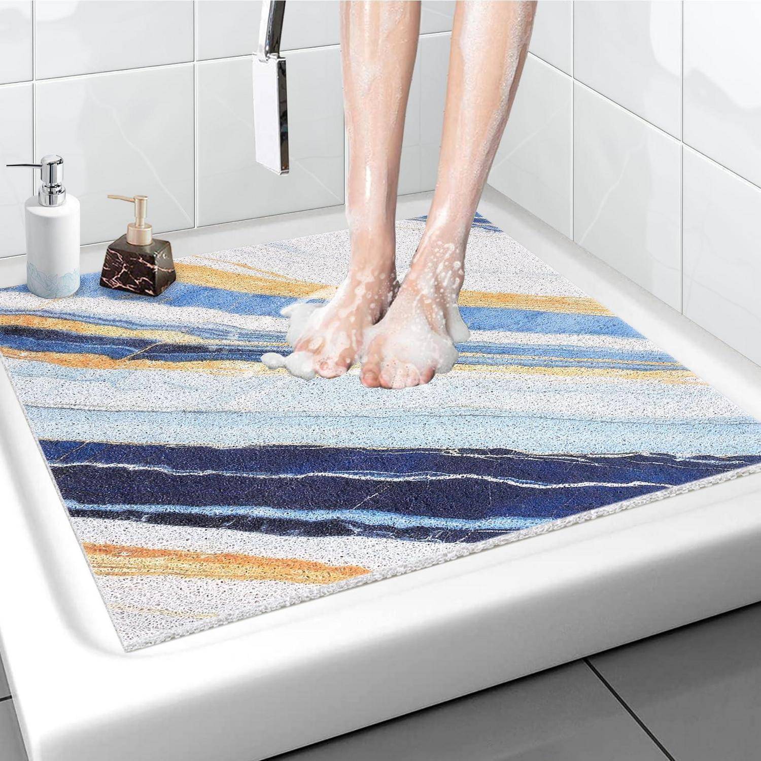Person wäscht sich die Füße in einer Dusche, steht auf einer farbenfrohen gestreiften Badevorleger in einem weiß gefliesten Badezimmer.