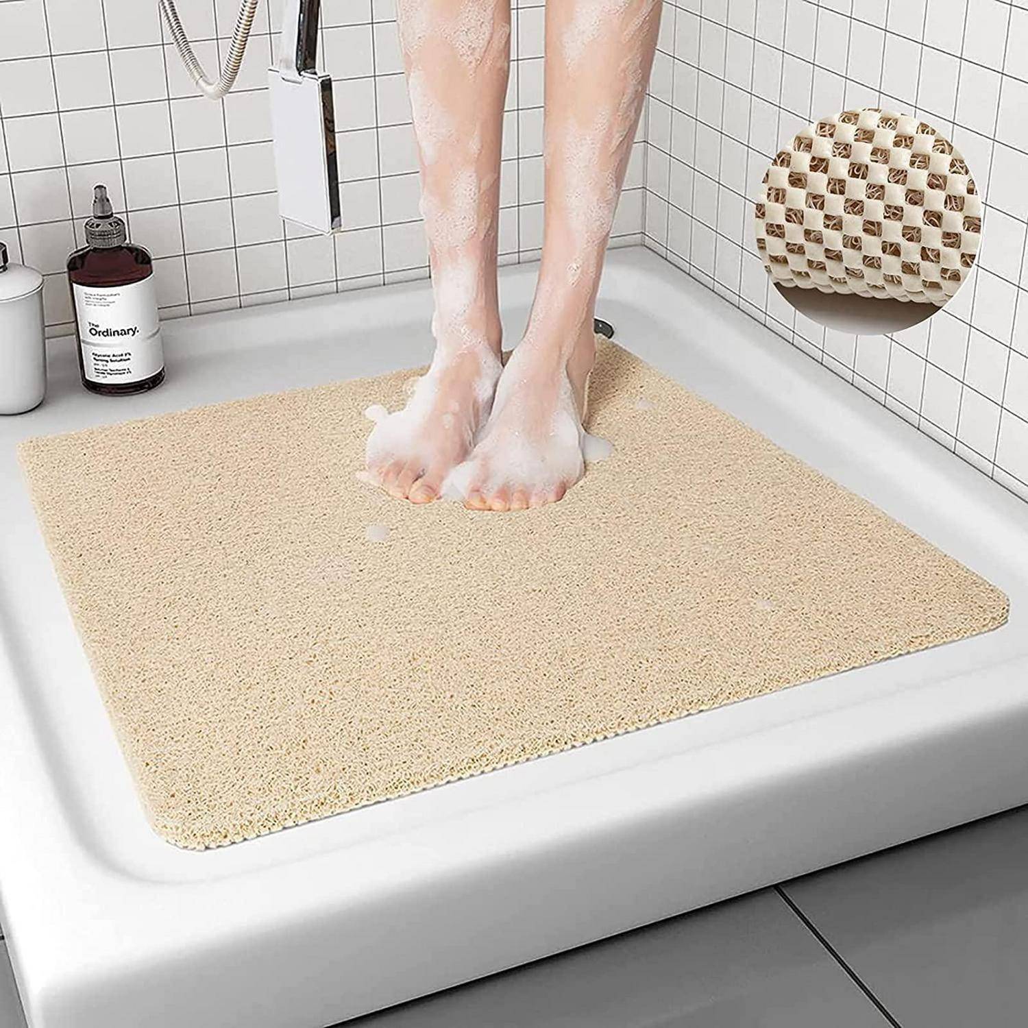 Füße stehen auf einer beigen Badematte in einer weiß gefliesten Badewanne, mit Seife und einer Flasche auf dem Rand.