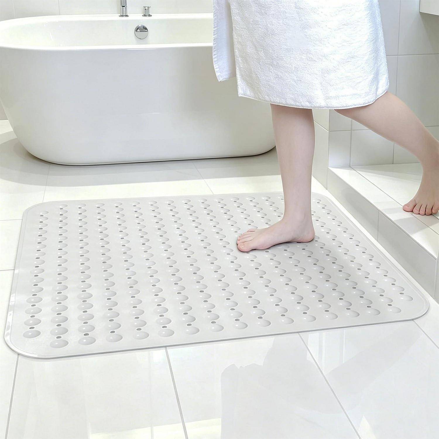 Eine Person steigt aus einer Badewanne auf eine weiße rutschfeste Badematte in einem gefliesten Badezimmer.