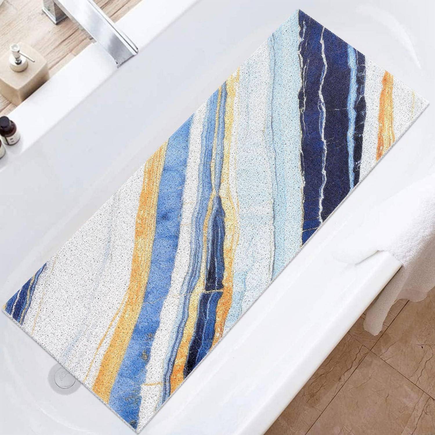 Abstrakter rechteckiger Teppich mit blauen, goldenen und weißen vertikalen Streifen auf einem Badezimmerboden neben einer Badewanne.