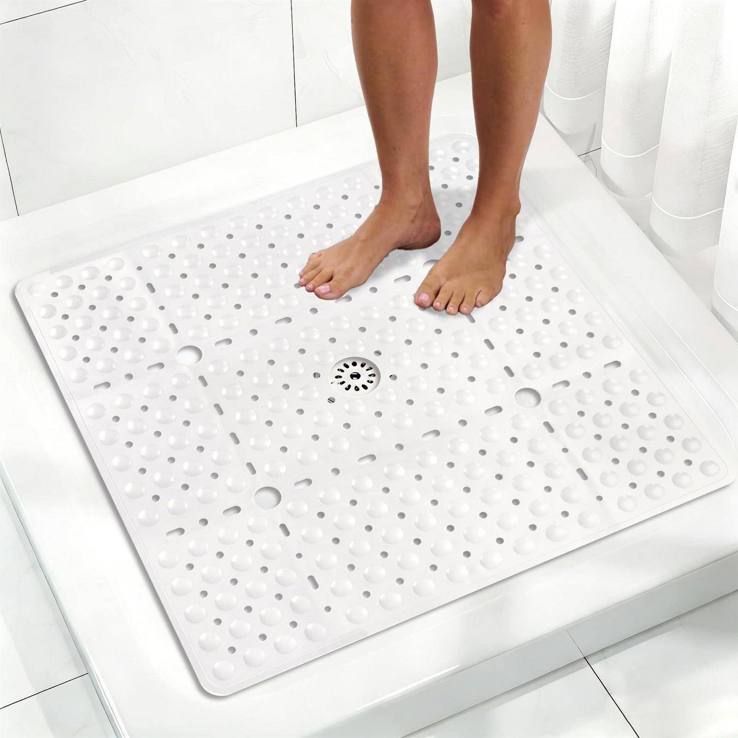 Nackte Füße stehen auf einer weißen strukturierten Duschmatte in einer begehbaren Dusche neben dem Ablauf.