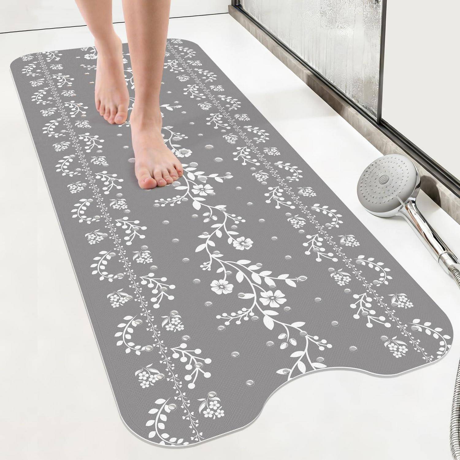 Nackte Füße treten auf eine blumenmusterierte graue Badematte neben einer Badewanne und einem Handbrausekopf.