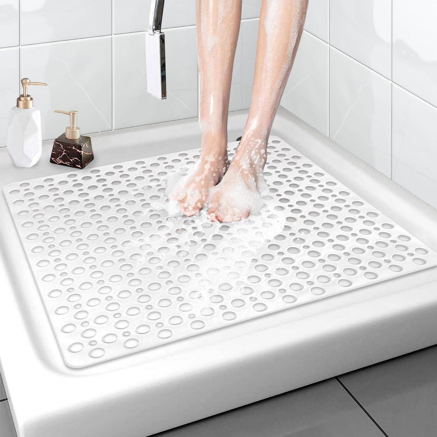 Person, die in einer Dusche auf einer weißen rutschfesten Badematte mit erhabener kreisförmiger Textur die Füße wäscht.