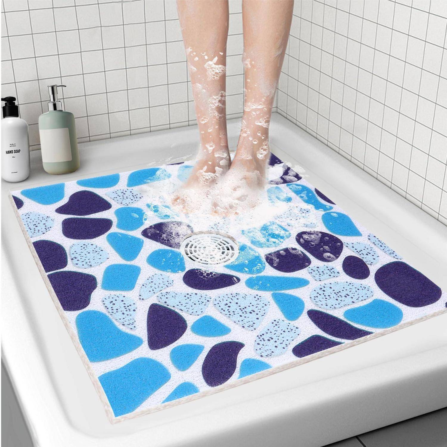 Eine Person steht auf einer farbigen rutschfesten Badewannenmatte unter der Dusche, während Wasser herabströmt, mit Seifenflaschen auf dem Rand.