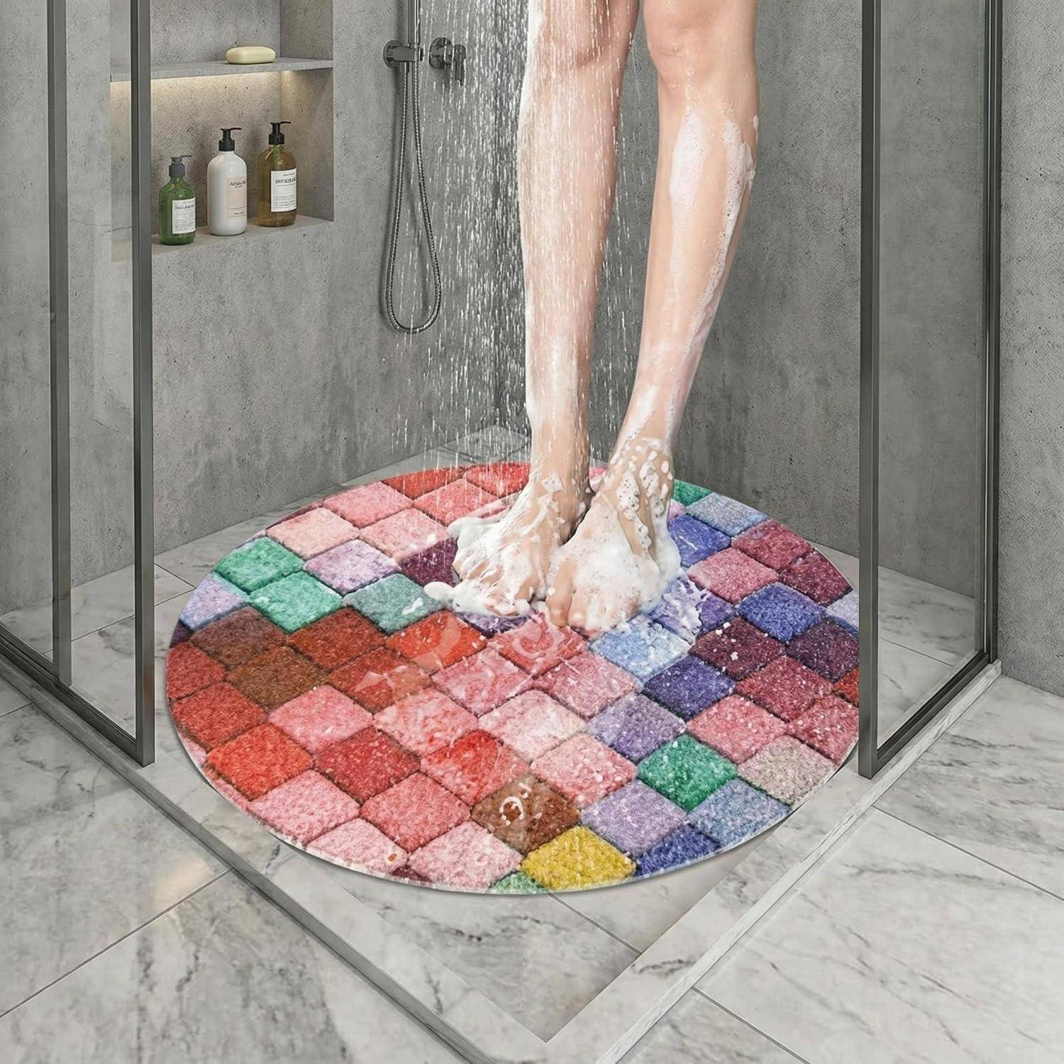 Person steht in einer gläsernen Dusche auf einer farbenfrohen runden Badmatte, mit Wasser, das über ihre Beine läuft.