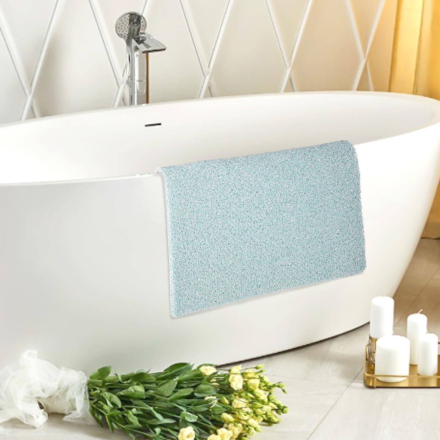 Modernes freistehende weiße Badewanne mit verchromter Duscharmatur, hellblau gefärbter Badmatte und Blumen sowie Kerzen auf dem Boden in einem hellen Badezimmer.