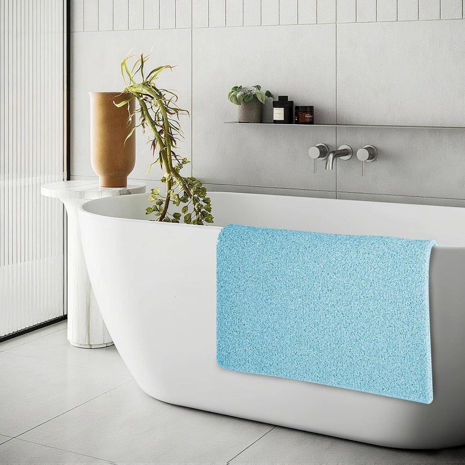 Modernes Badezimmer mit einer freistehenden weißen Badewanne, einem blauen Handtuch, das über die Seite drapiert ist, und einer Pflanze auf einem Podest daneben.