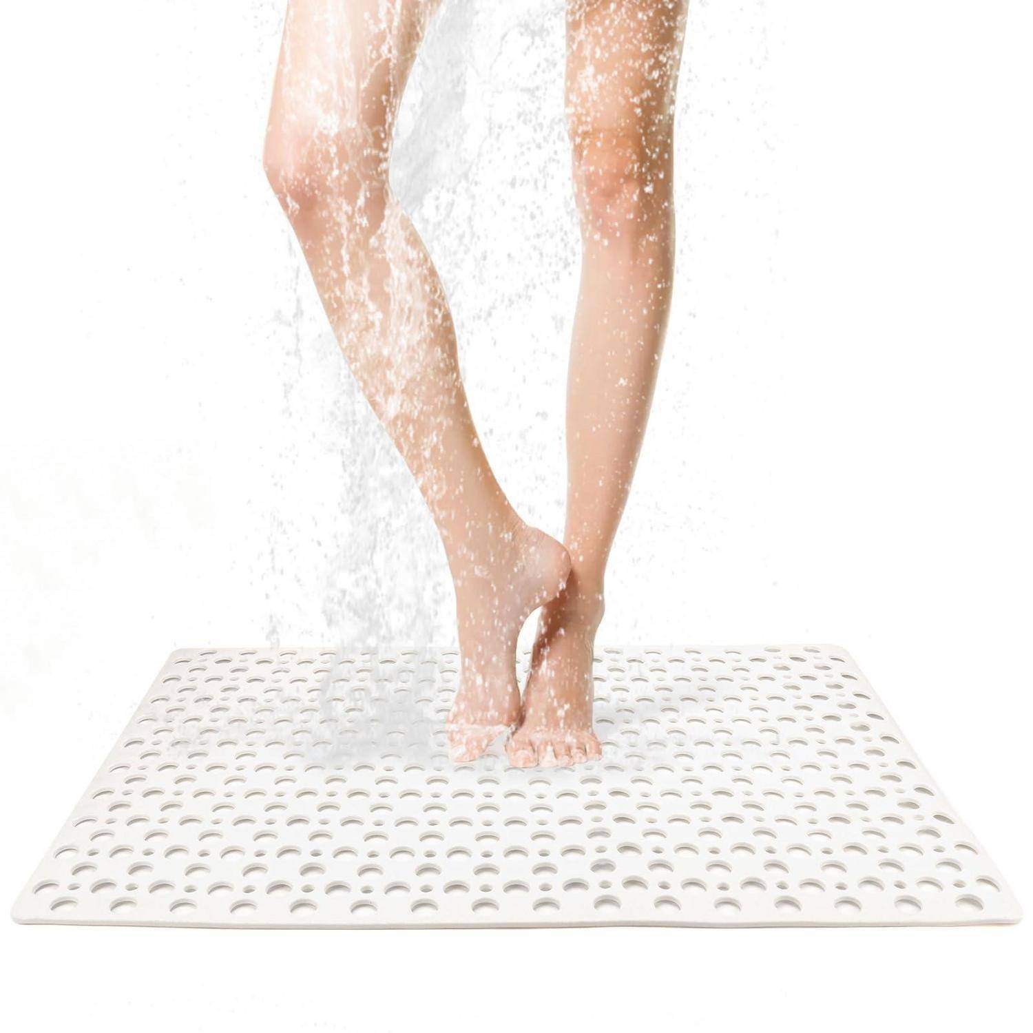 Nahaufnahme von nackten Beinen, die auf einer weißen perforierten Duschmatte unter fließendem Wasser stehen, was auf ein Duschsicherheits- oder Fußpflegeprodukt hindeutet.