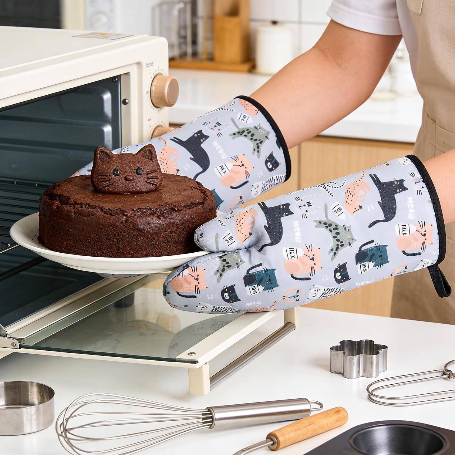 Eine Person trägt katzengemusterte Ofenhandschuhe und nimmt einen Schokoladenkuchen mit einer katzenförmigen Oberseite aus einem offenen Ofen.