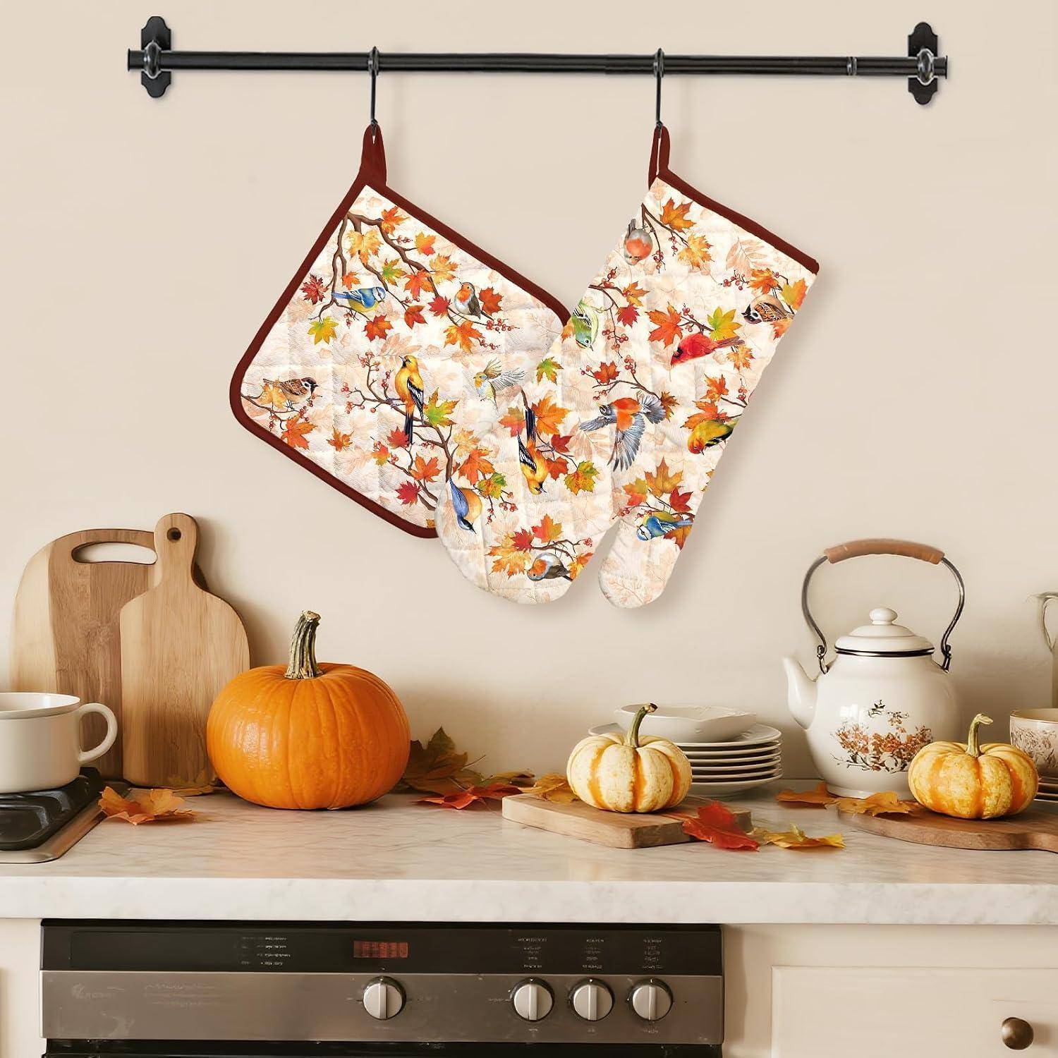 Herbstliche Küchensszene mit floralen Ofenhandschuhen, die über einer Theke hängen, auf der Kürbisse, Schneidbretter, Geschirr und eine Teekanne ausgestellt sind.