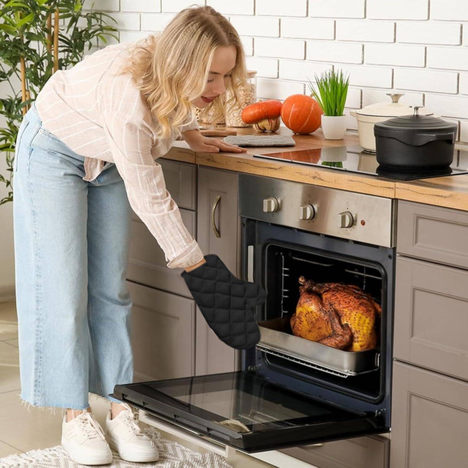 Eine Frau in einer Küche öffnet einen Ofen mit einem gebratenen Huhn darin, verwendet einen Ofenhandschuh und überprüft das Essen.