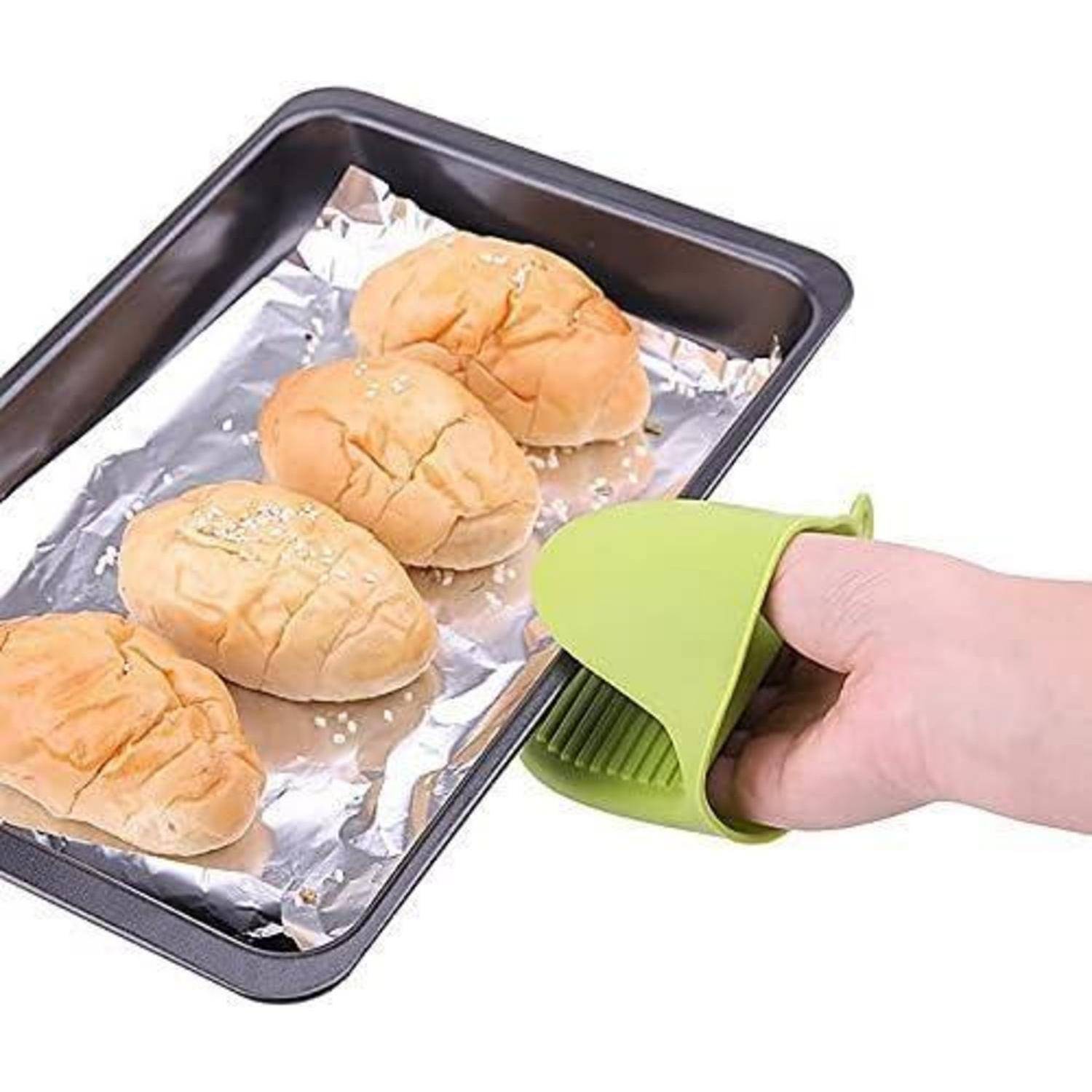 Hand mit einem grünen Silikon-Ofenhandschuh, der ein heißes Backblech mit Folie und fünf Brötchen hält.