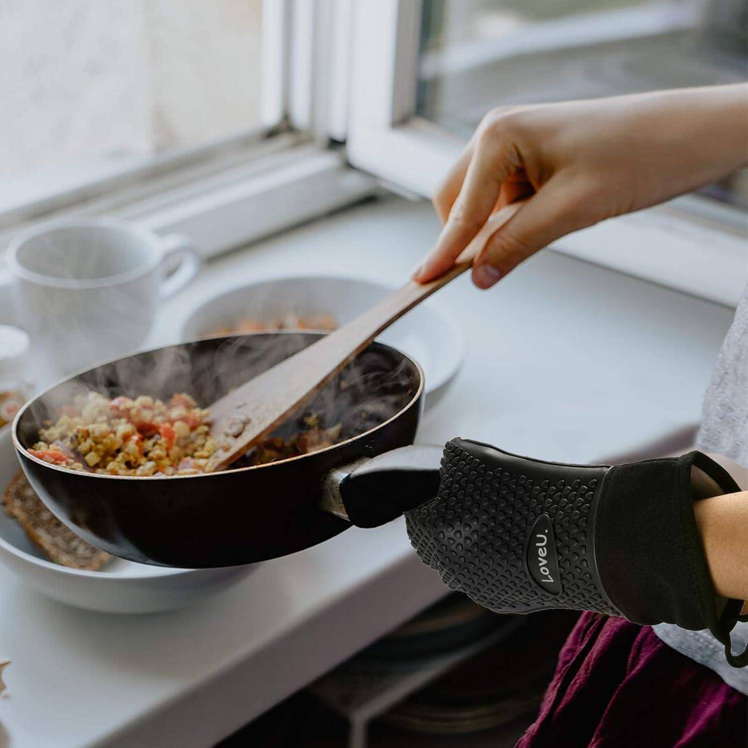 Eine Person rührt dampfende Lebensmittel in einer Pfanne auf der Fensterbank um, während sie einen Ofenhandschuh trägt und den Griff für sicheres Kochen hält.