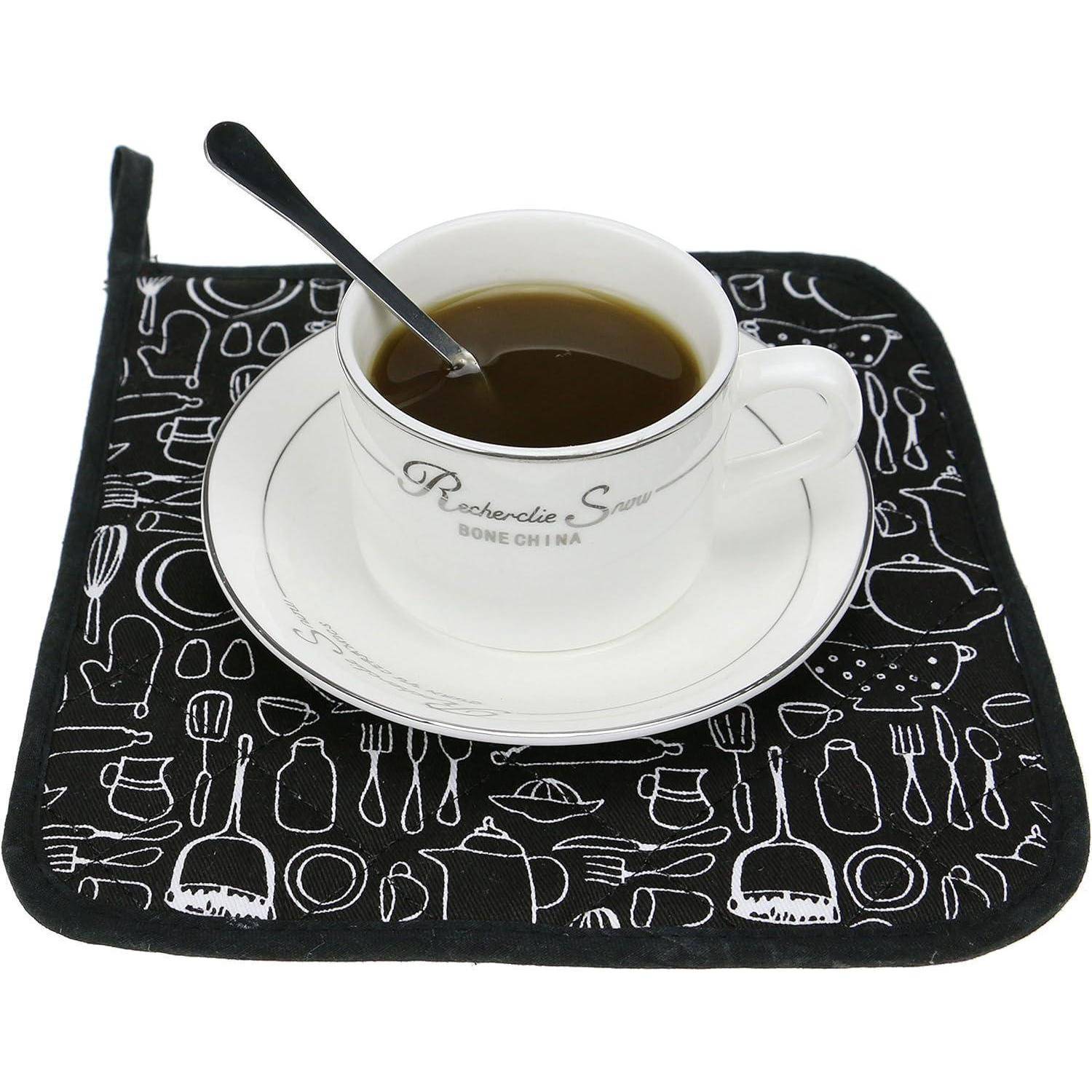 Weiße Teetasse mit dunklem Kaffee und Löffel auf einer Untertasse, gestellt auf einer schwarz gemusterten Serviette.