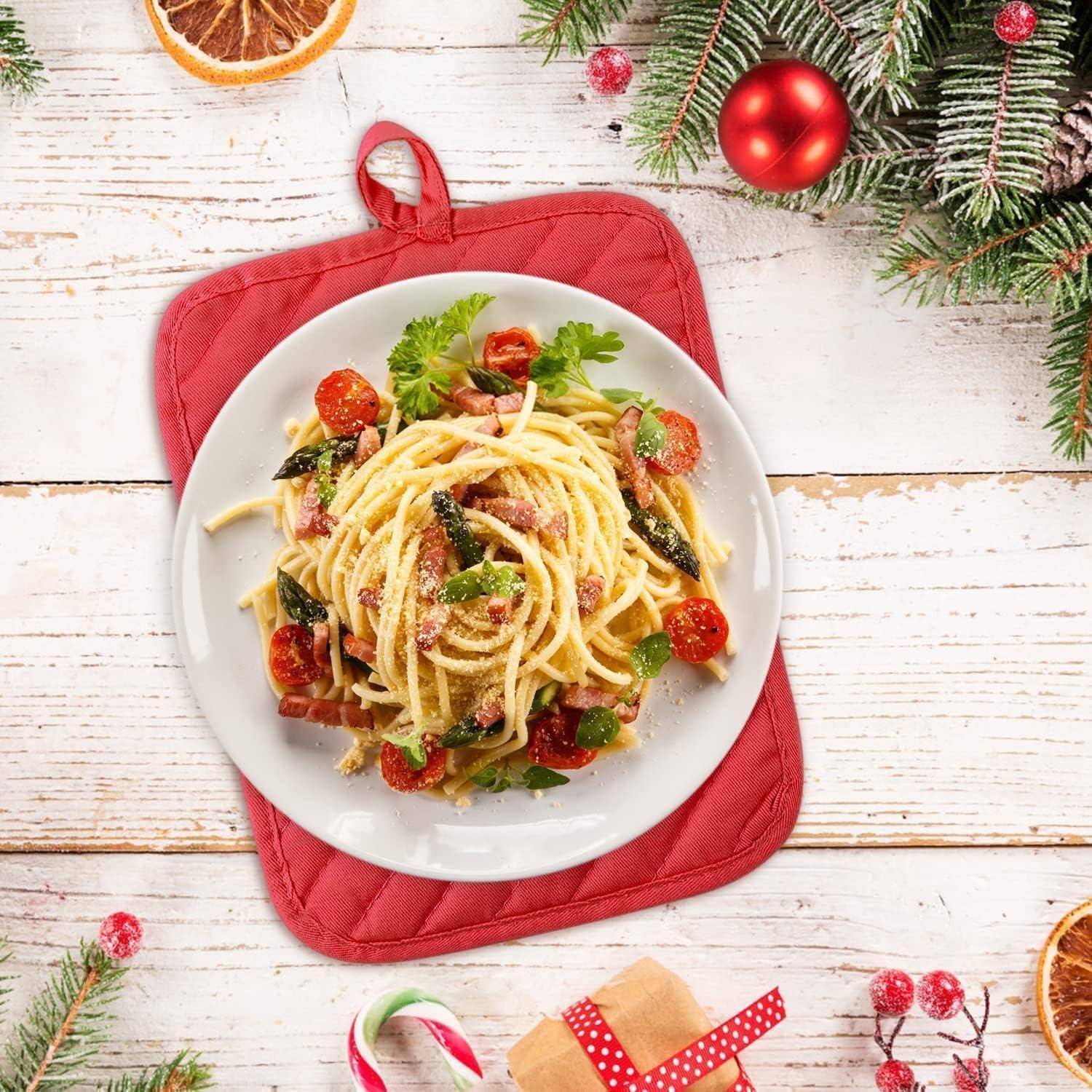 Teller mit Spaghetti, Kirschtomaten und Basilikum auf einem roten Topflappen, umgeben von festlichen Weihnachtsdekorationen auf einem weißen Holztisch.
