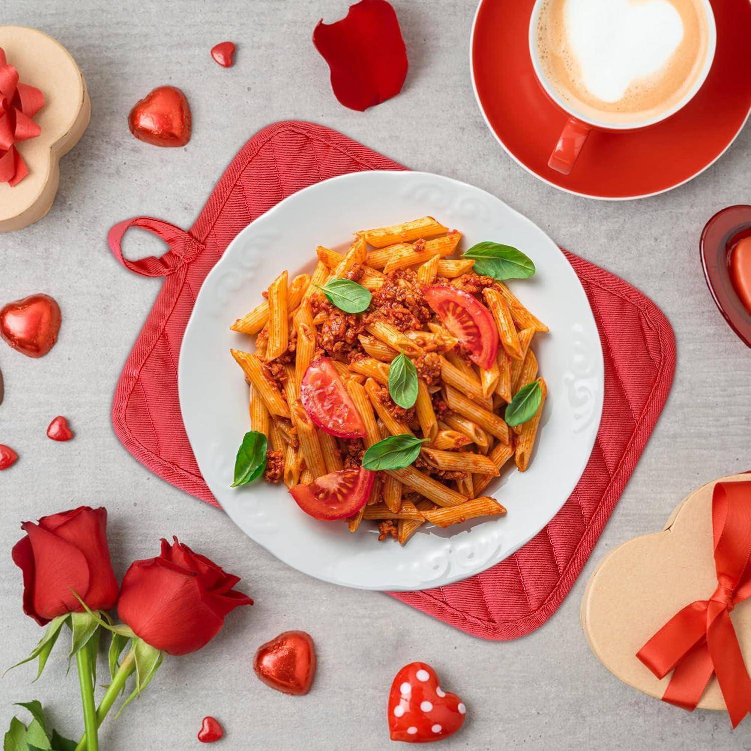 Teller mit Penne-Pasta in Tomatensoße und Basilikum auf einem roten Platzdeckchen, umgeben von roten Rosen, Herzdekorationen und einer Tasse Kaffee.