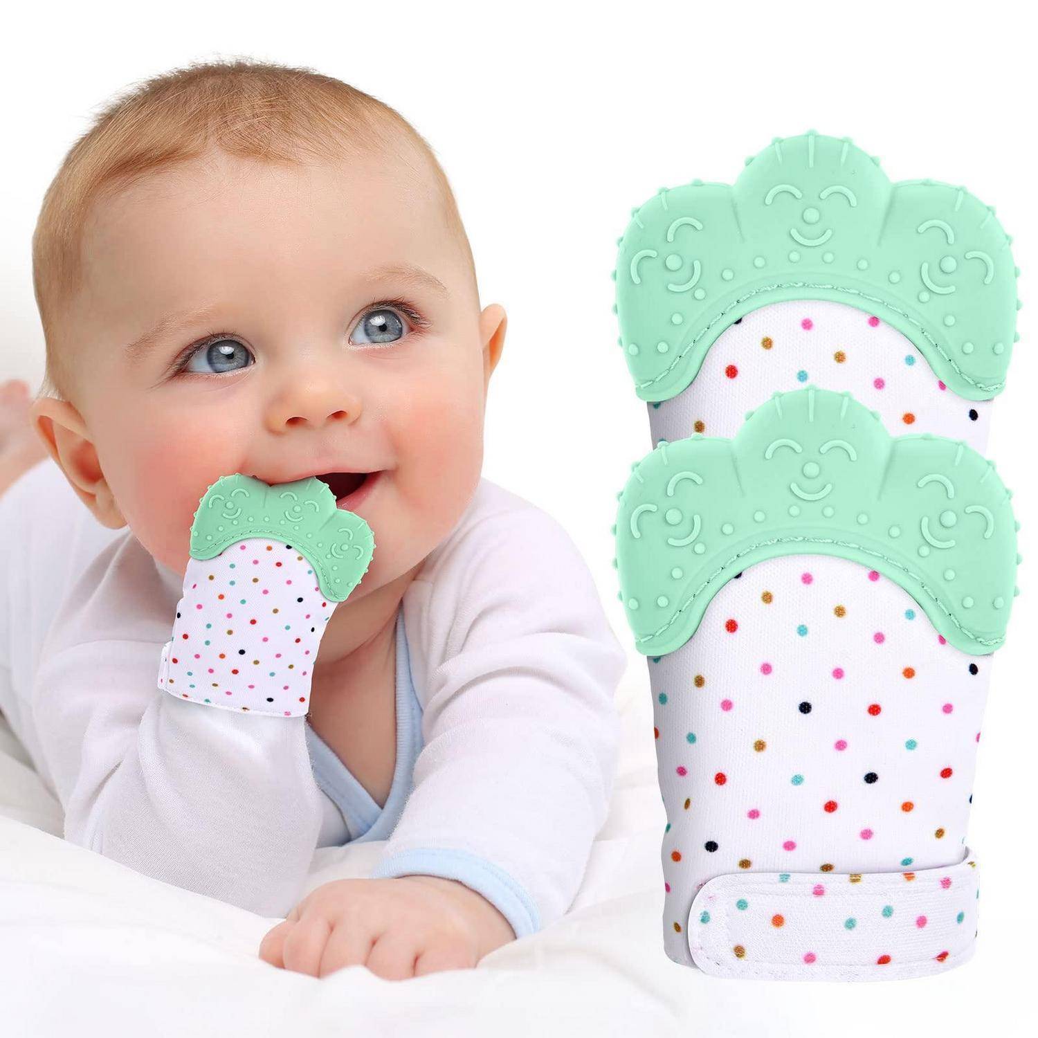 Baby auf weißer Bettwäsche, das an einem mintgrünen Beißhandschuh mit Punktmuster kaut, wobei ein passender Handschuh daneben gezeigt wird.