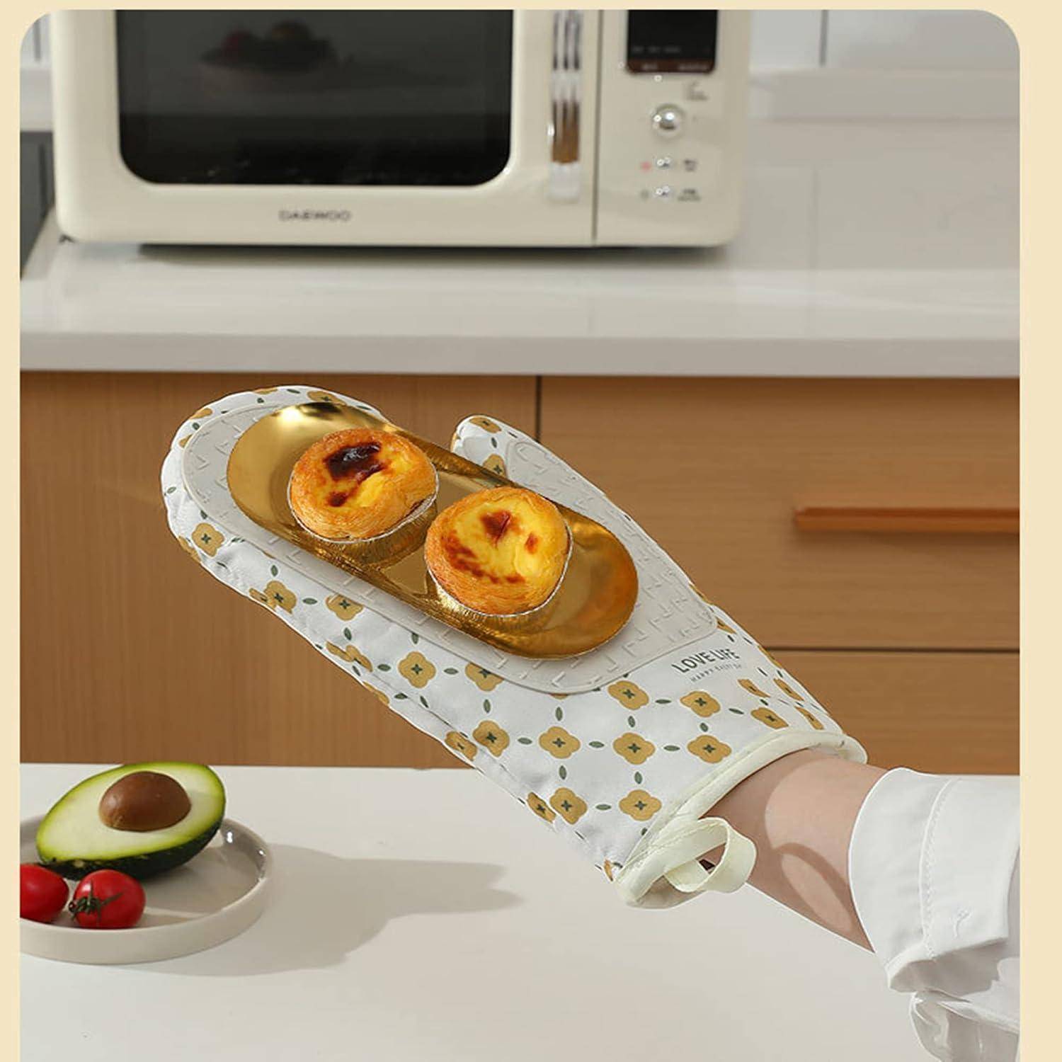 Eine Person mit einem Ofenhandschuh hält ein goldenes Tablett mit zwei gebackenen Pfirsichgebäcken in einer Küche, mit Avocado und Kirschtomaten auf der Arbeitsfläche.