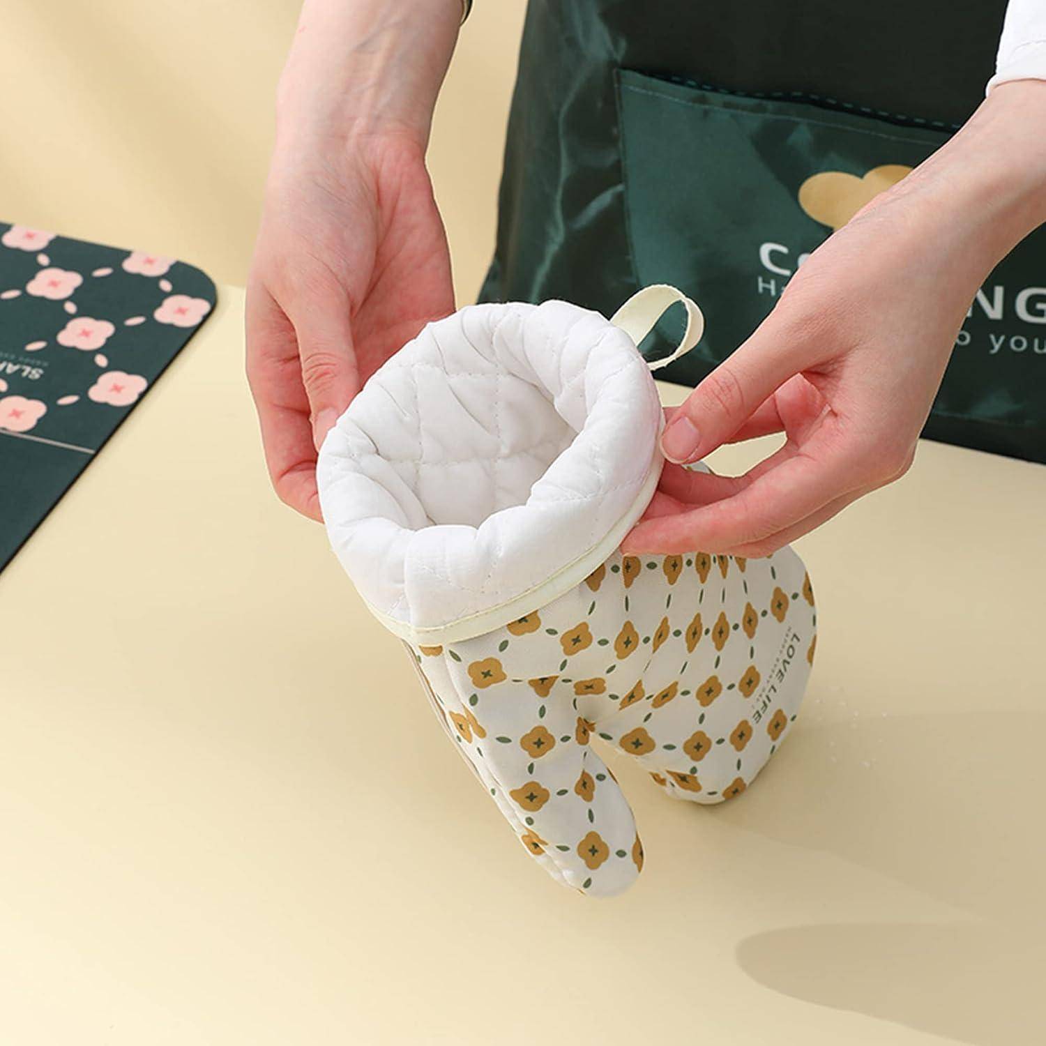 Hände halten eine kleine gesteppte Babymütze mit Ohrenklappen auf einer Tischplatte, die ein weiße gepolsterte Innenfütterung und gemustertem Außenstoff zeigt.
