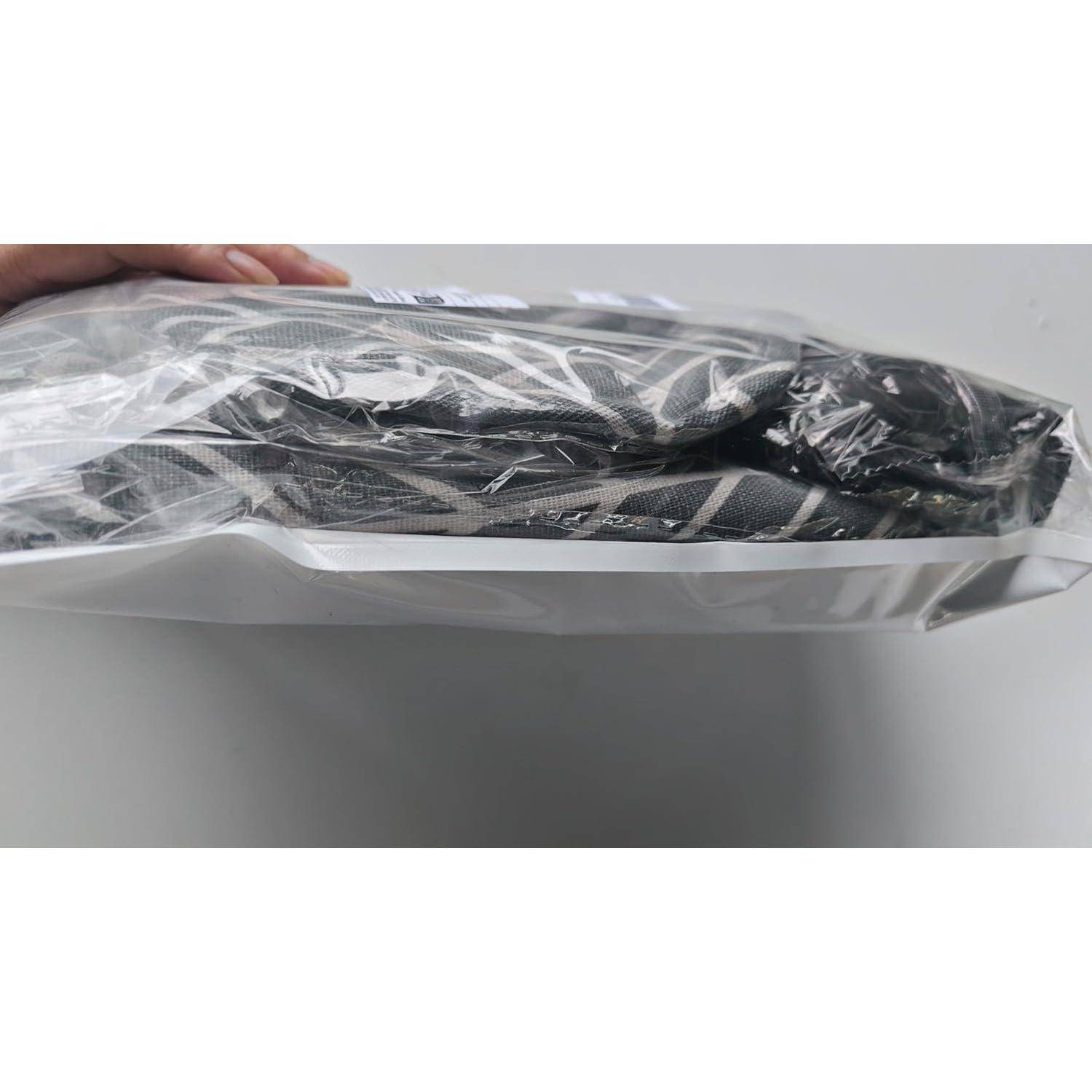 Ein gefaltetes schwarzes Kleidungsstück in einer durchsichtigen Plastiktüte, von der Seite auf einer weißen Oberfläche betrachtet.