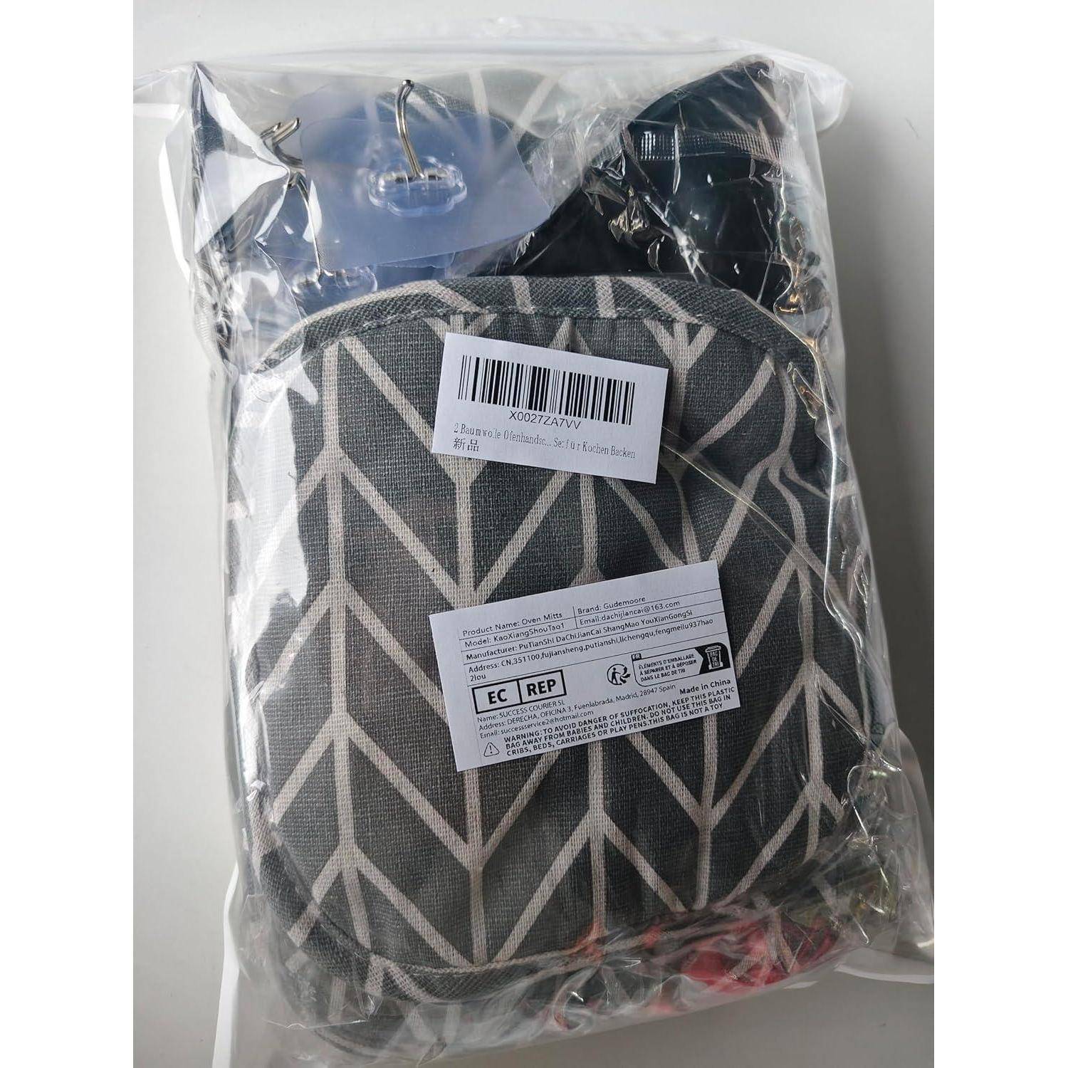 Eine gemusterte grau-weiße Tasche in einer durchsichtigen Kunststoffhülle verpackt, mit Barcode und Produktetiketten angebracht.