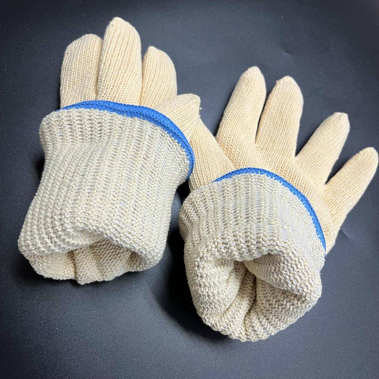 Paar beige gestrickte Arbeitshandschuhe mit blauen Bündchen auf einer dunklen Oberfläche, wobei die Handschuhe gefaltet und nebeneinander gestapelt gezeigt werden.
