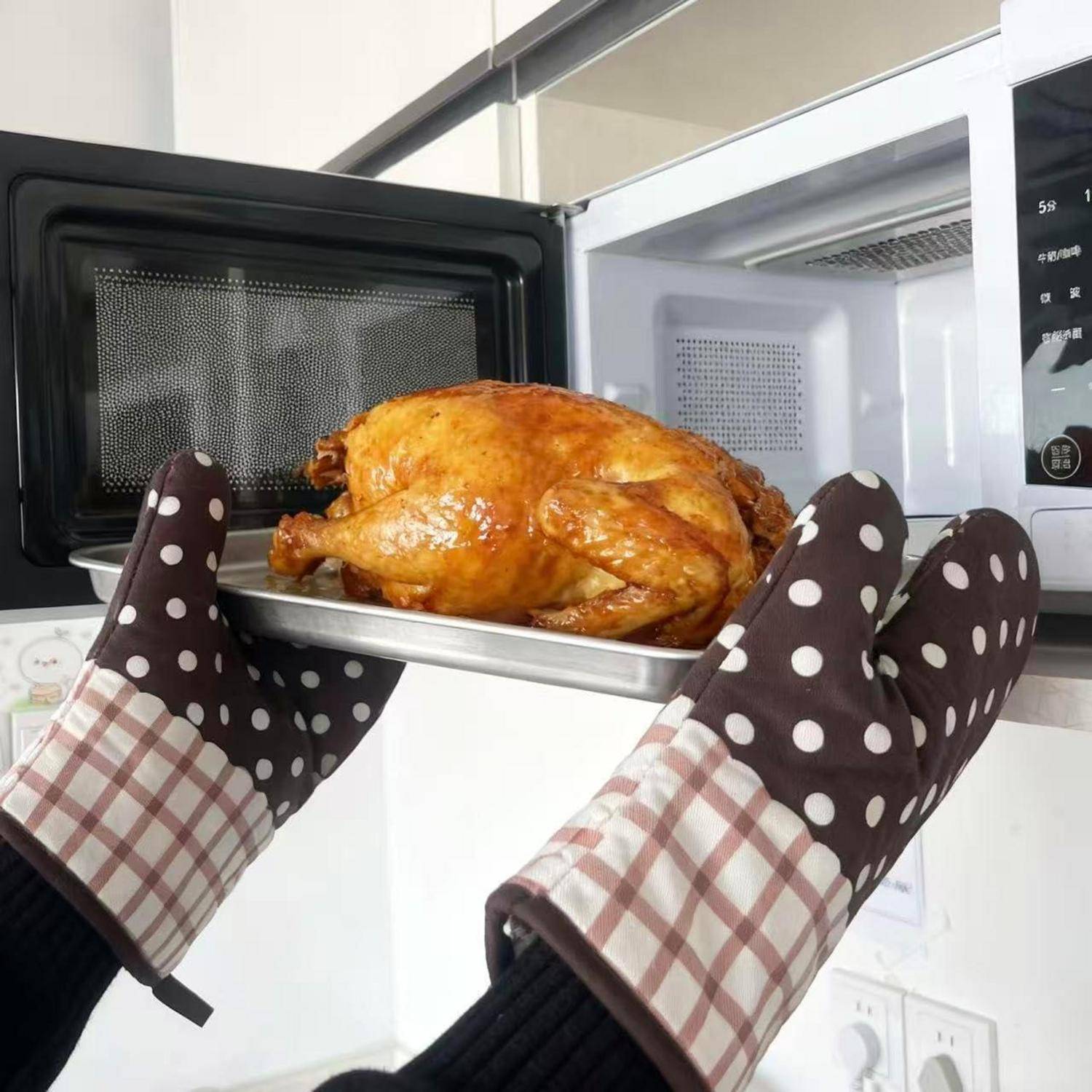 Behandschuhte Hände nehmen ein gebratenes ganzes Huhn auf einem Tablett aus einer Mikrowelle.