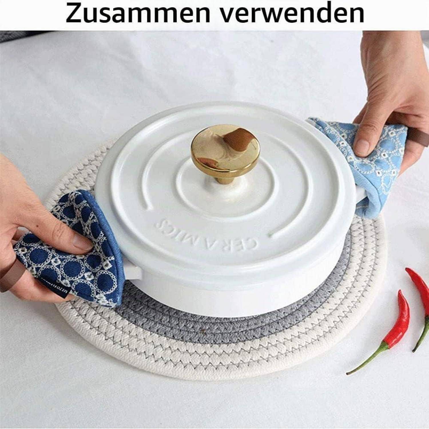 Hände verwenden blaue Topflappen, um einen weißen Topf mit Deckel von einem geflochtenen Untersetzer zu heben; der deutsche Text lautet „Zusammen verwenden