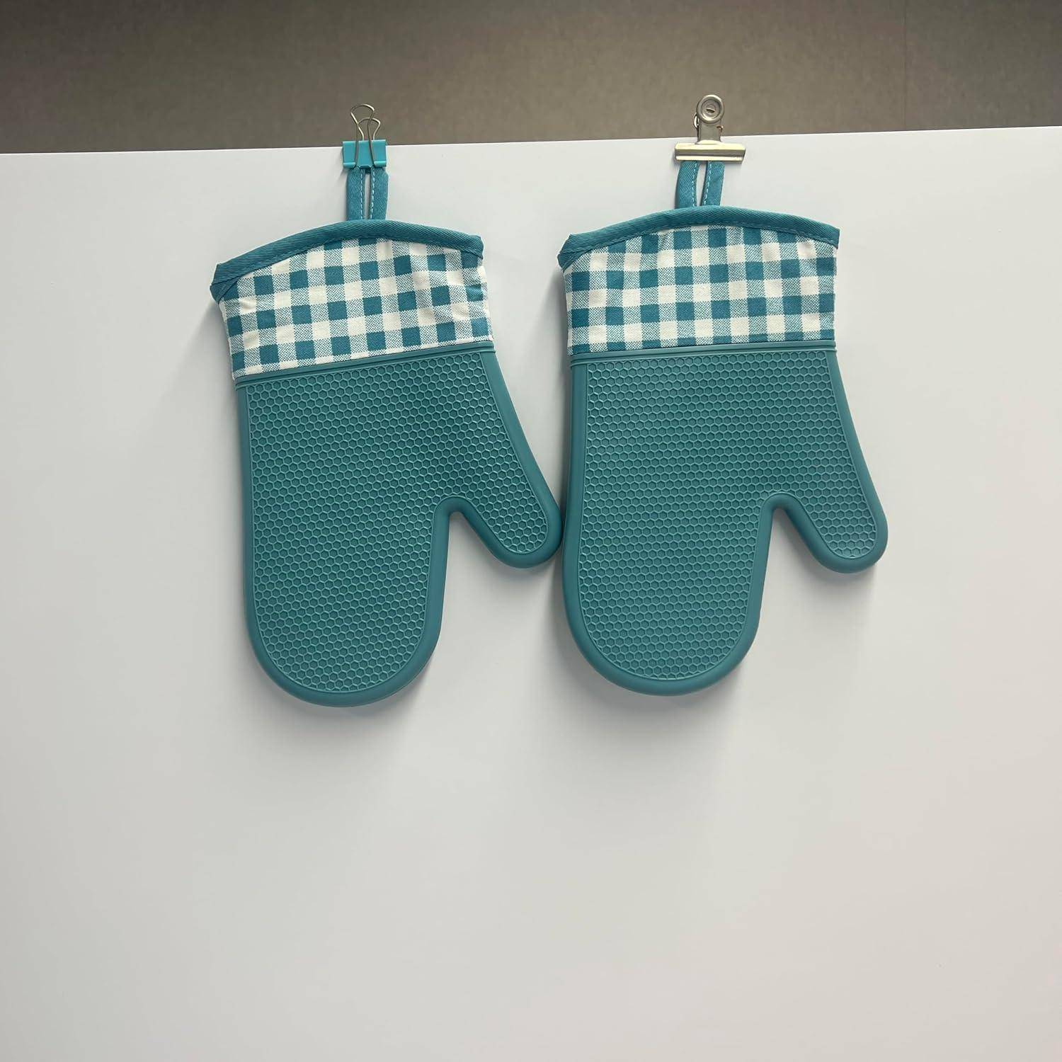 Paar türkisfarbener Ofenhandschuhe mit blau-weißen karierten Manschetten, die nebeneinander an Haken an einer hellen Wand hängen.