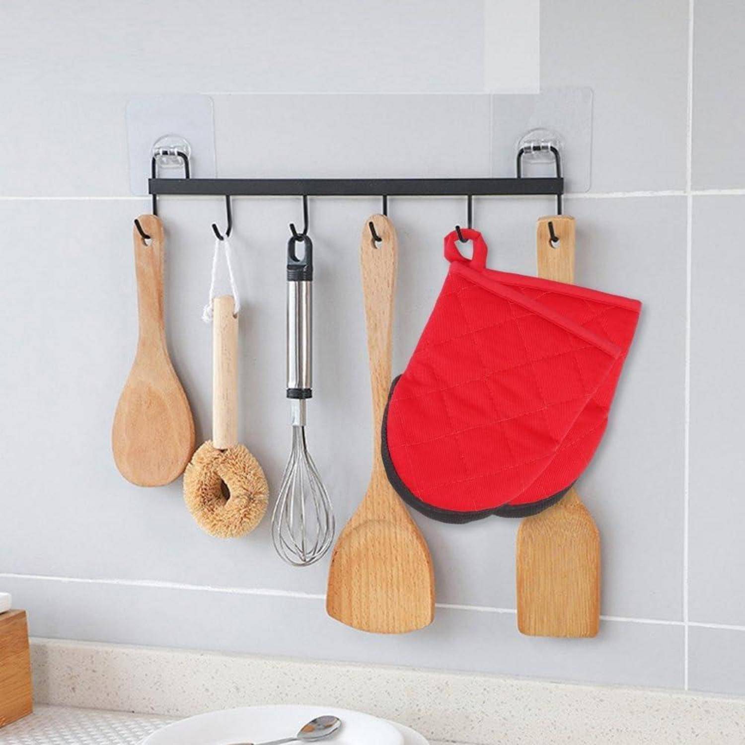 Küchengerätehalter an gekachelter Wand mit Holzlöffeln, einem Schneebesen, einer Spülbürste und einem roten Ofenhandschuh.