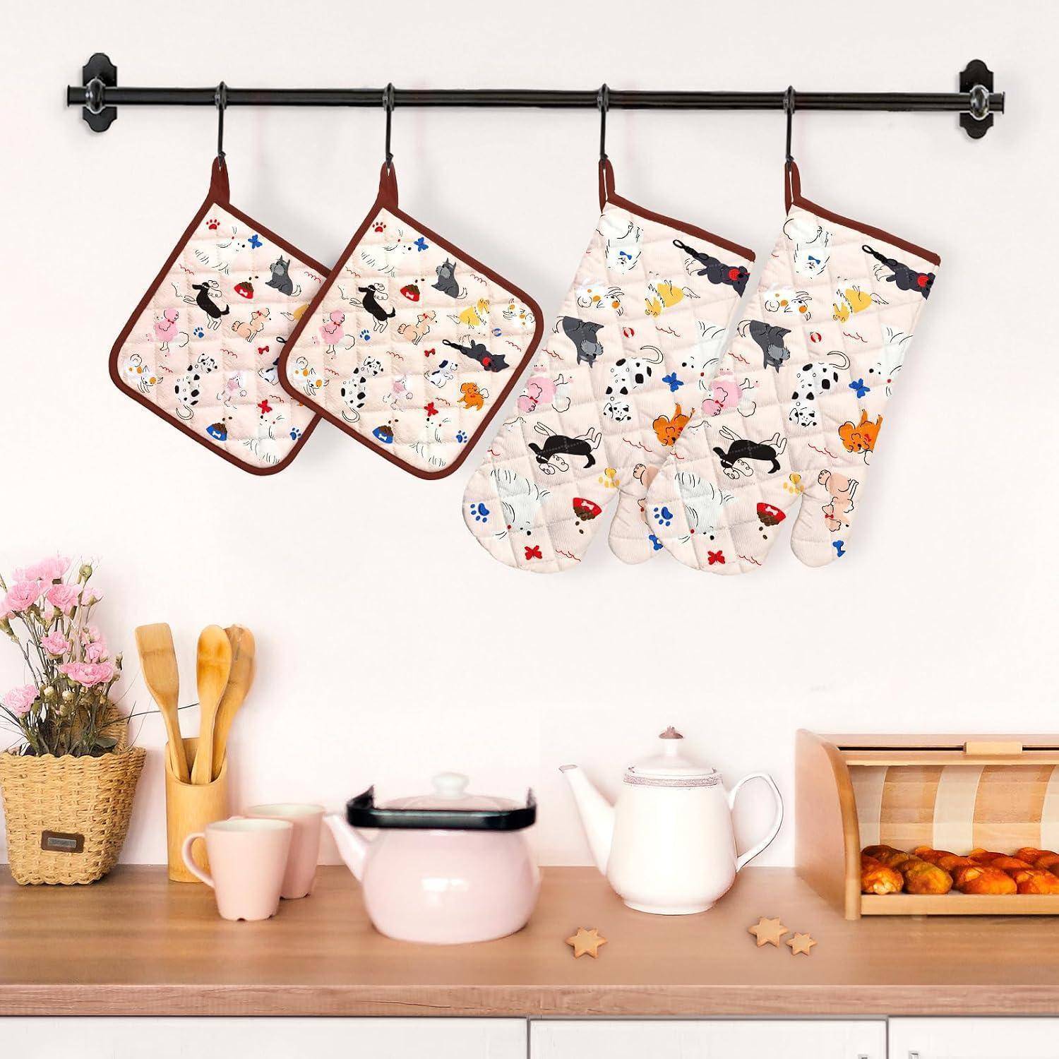Küchenregal an der Wand mit zwei hängenden Topflappen und zwei Ofenhandschuhen über einer Arbeitsplatte mit einem Wasserkessel, Tassen, Küchenutensilien, Blumen und einer Brotbox.
